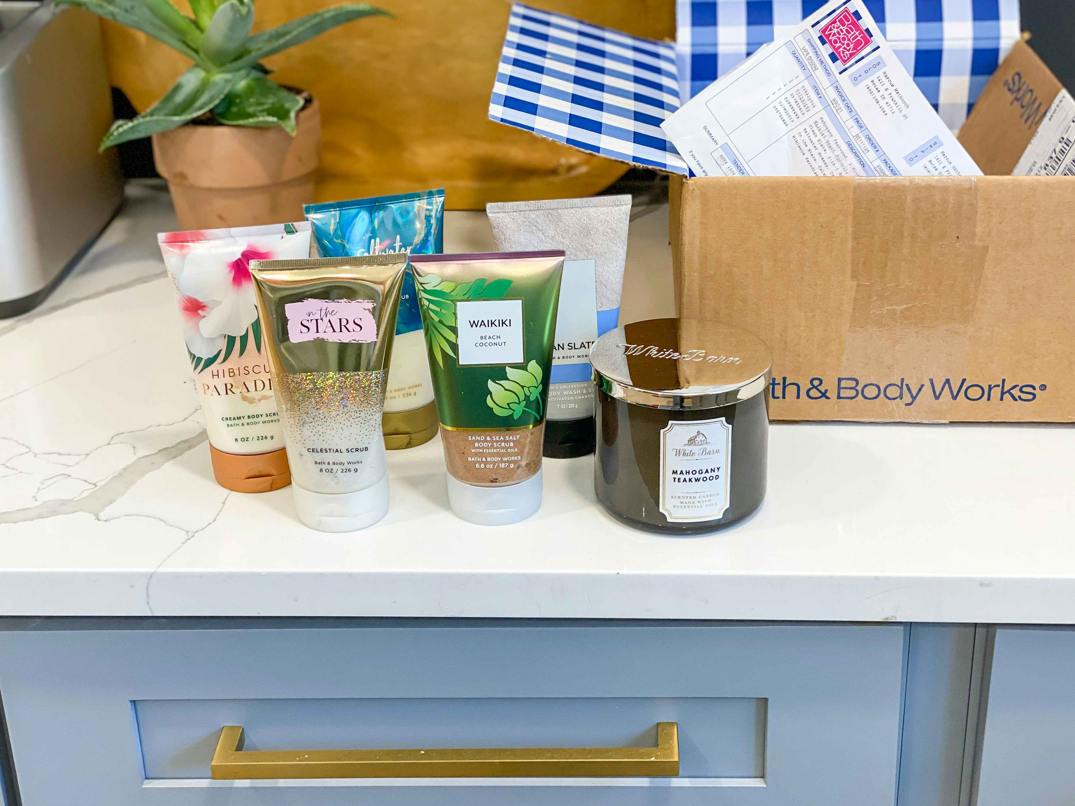 body lotions and a three-wick candle on a countertop next to a Bath & Body Works shipping box