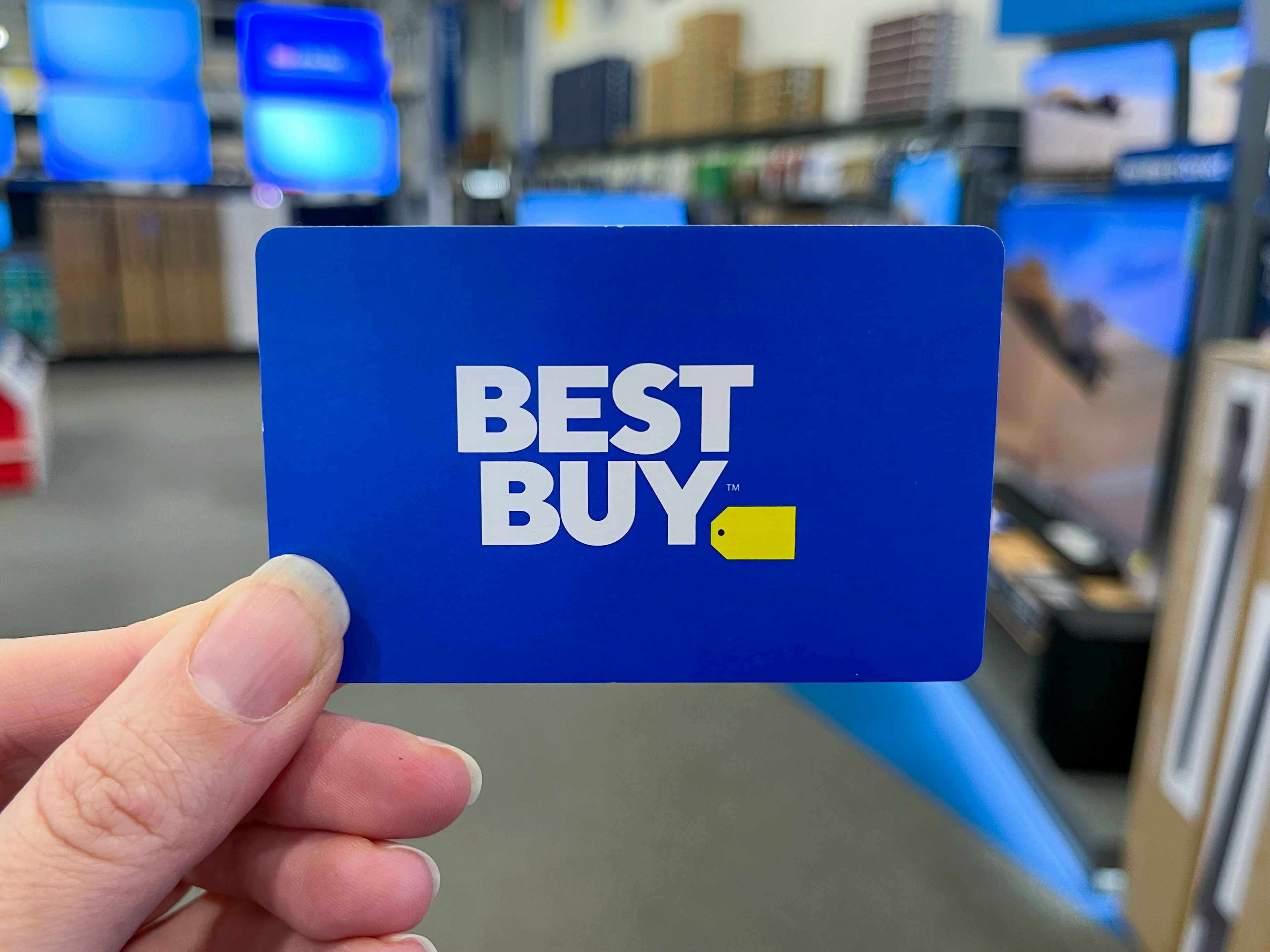 A person's hand holding a Best Buy gift card inside Best Buy.