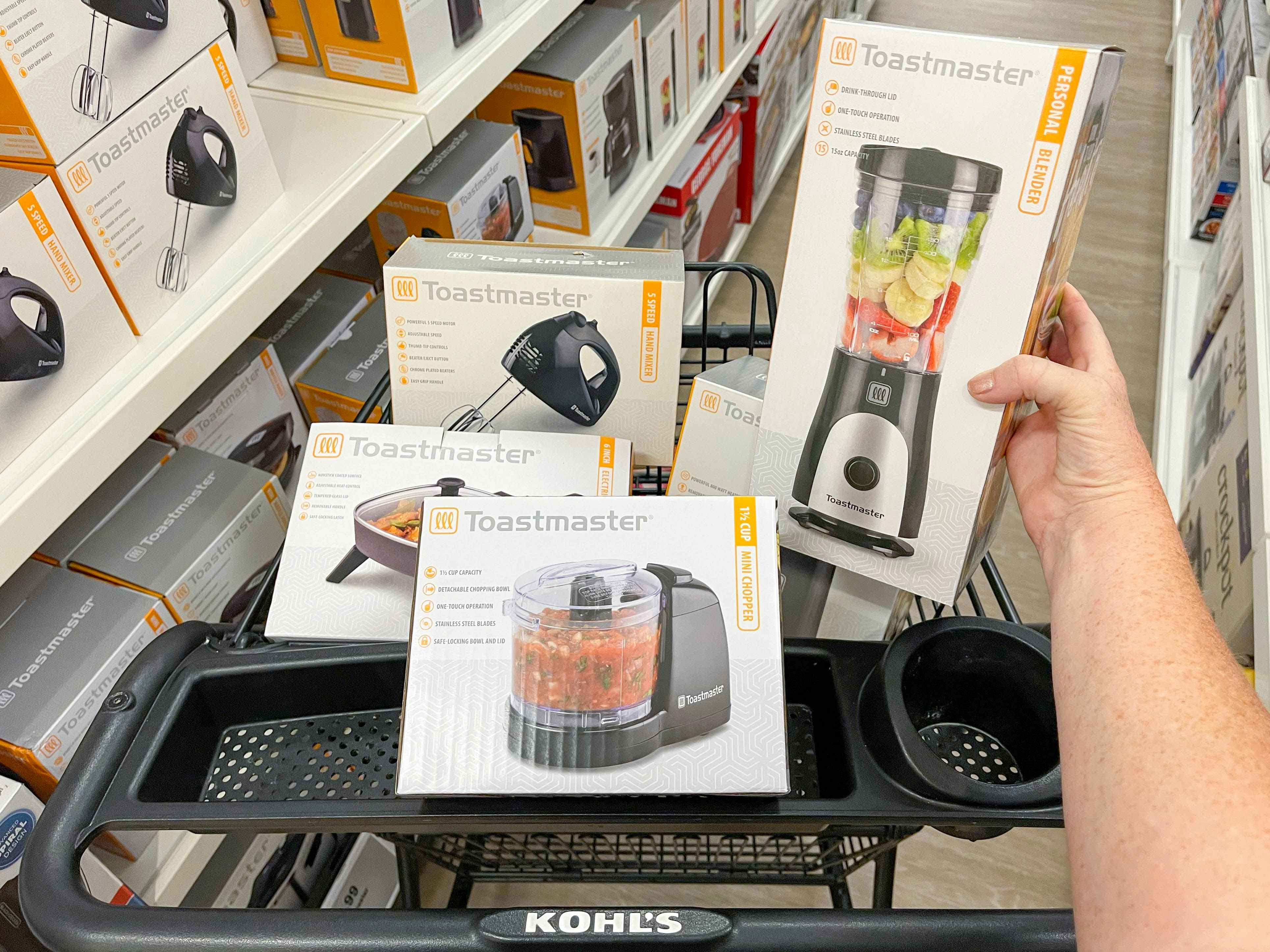 A person's hand holding a Toastmaster blender above more small Toastmaster appliances in a Kohl's shopping cart.