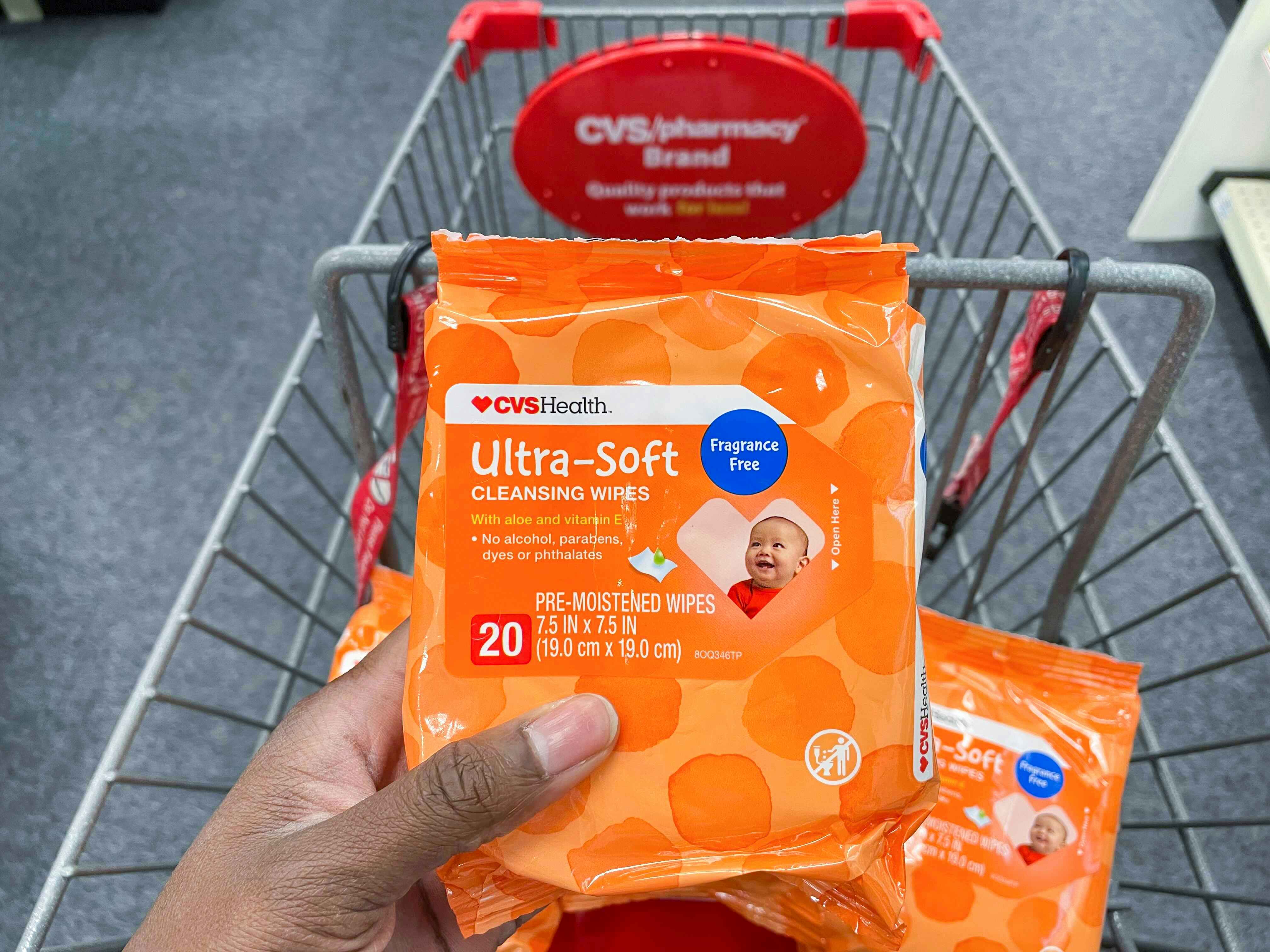A person's hand holding some CVS health baby wipes in front of a CVS cart.
