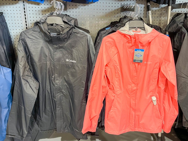 Columbia jackets hanging on racks. One is a mens in black, the other is a womans in coral.