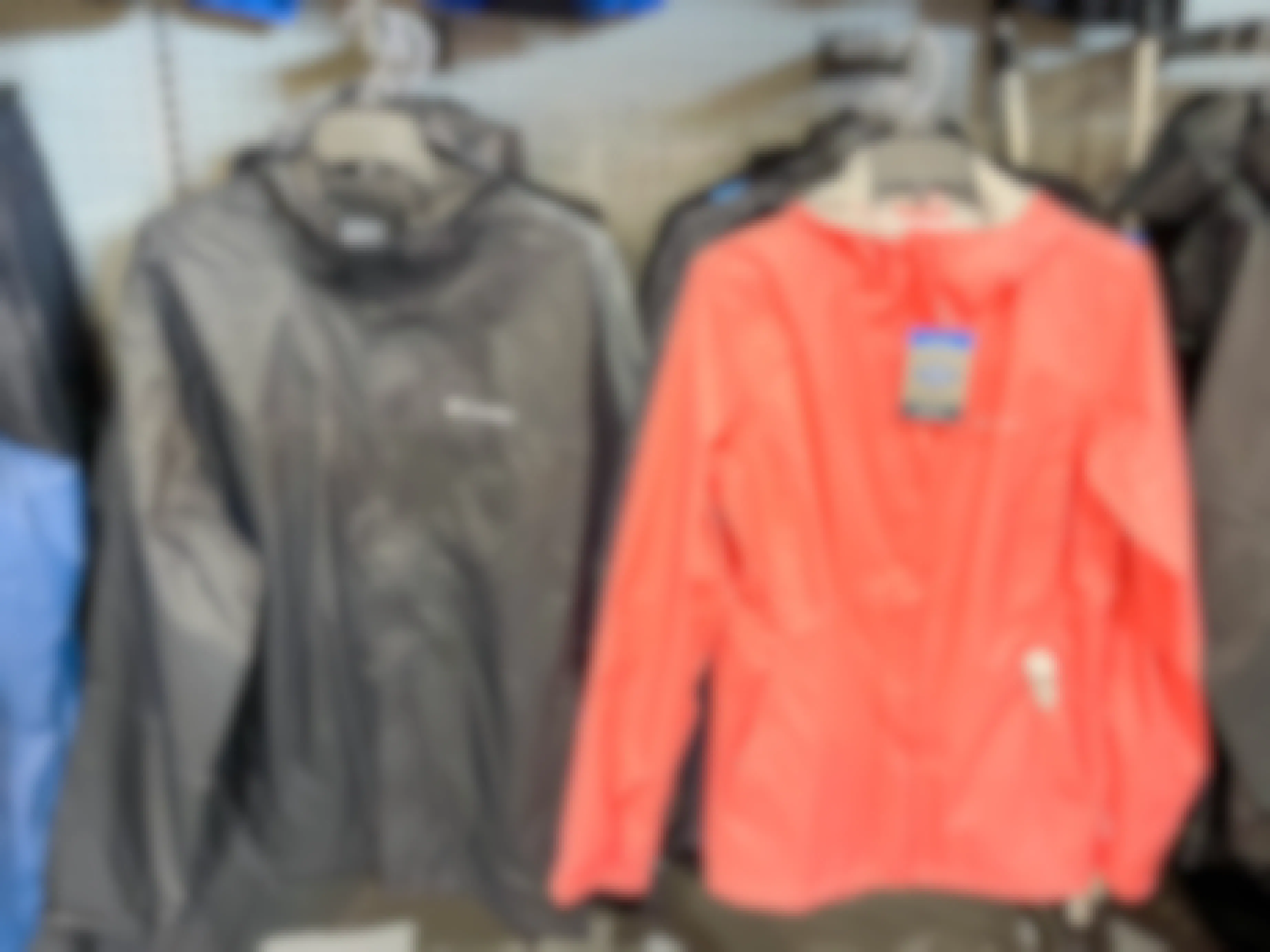 Columbia jackets hanging on racks. One is a mens in black, the other is a womans in coral.
