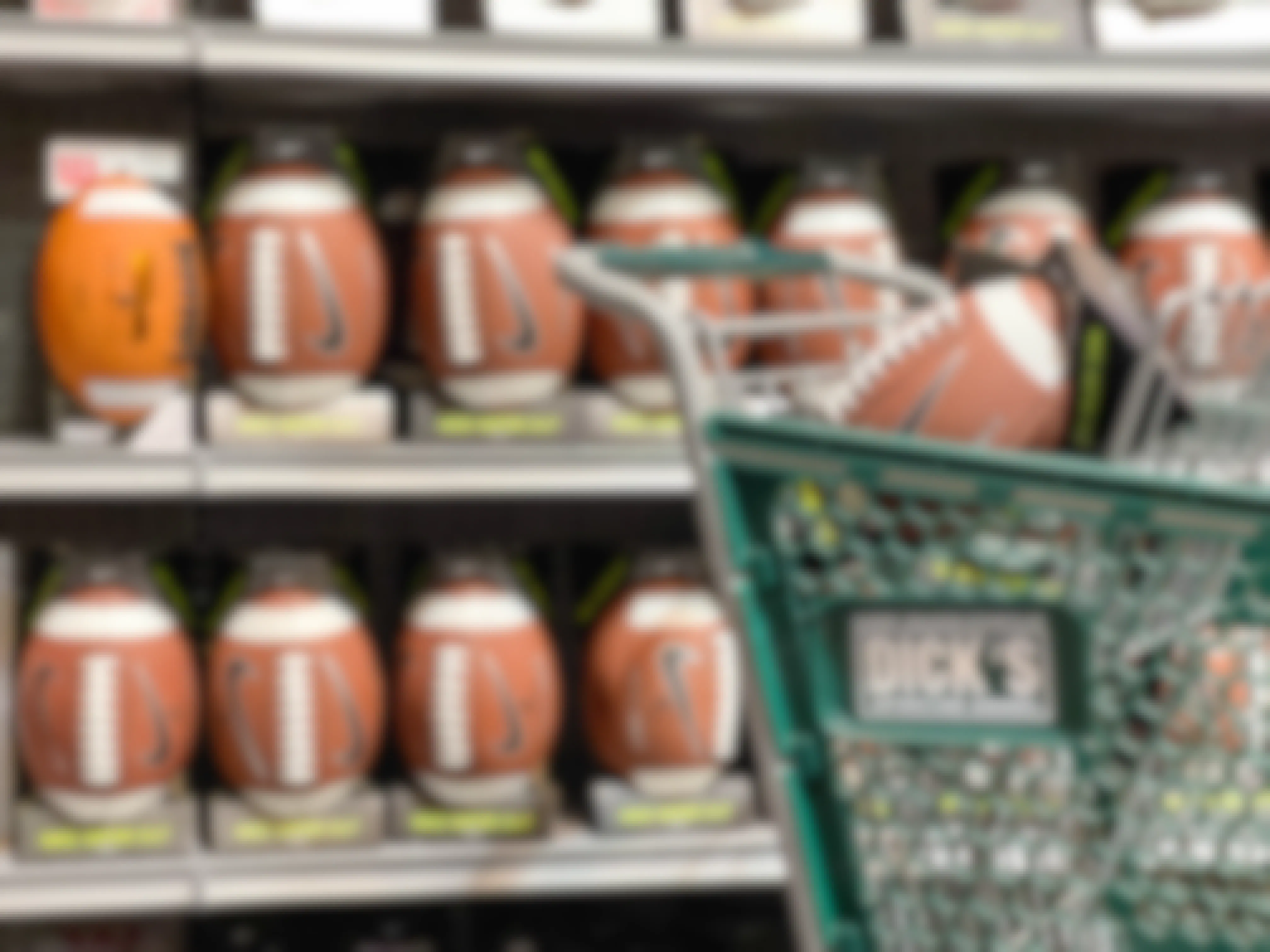 Footballs on a for sale shelf with one in a Dicks sporting goods shopping cart in the forground