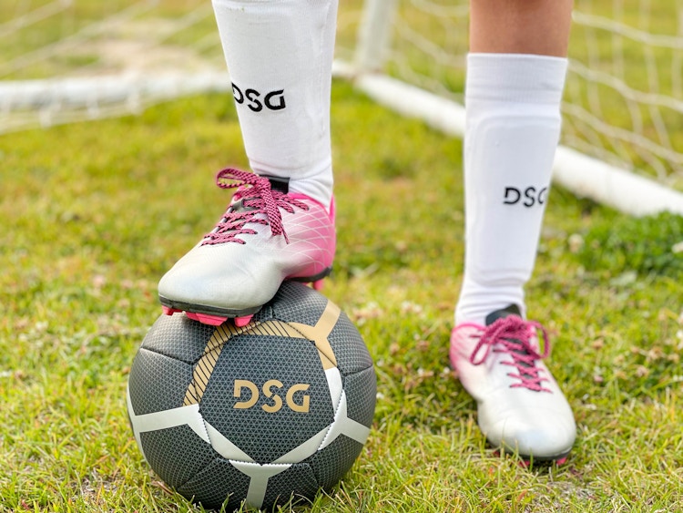 A child wearing DSG soccer shoes, socks, pads, stepping on a DSG soccer ball.