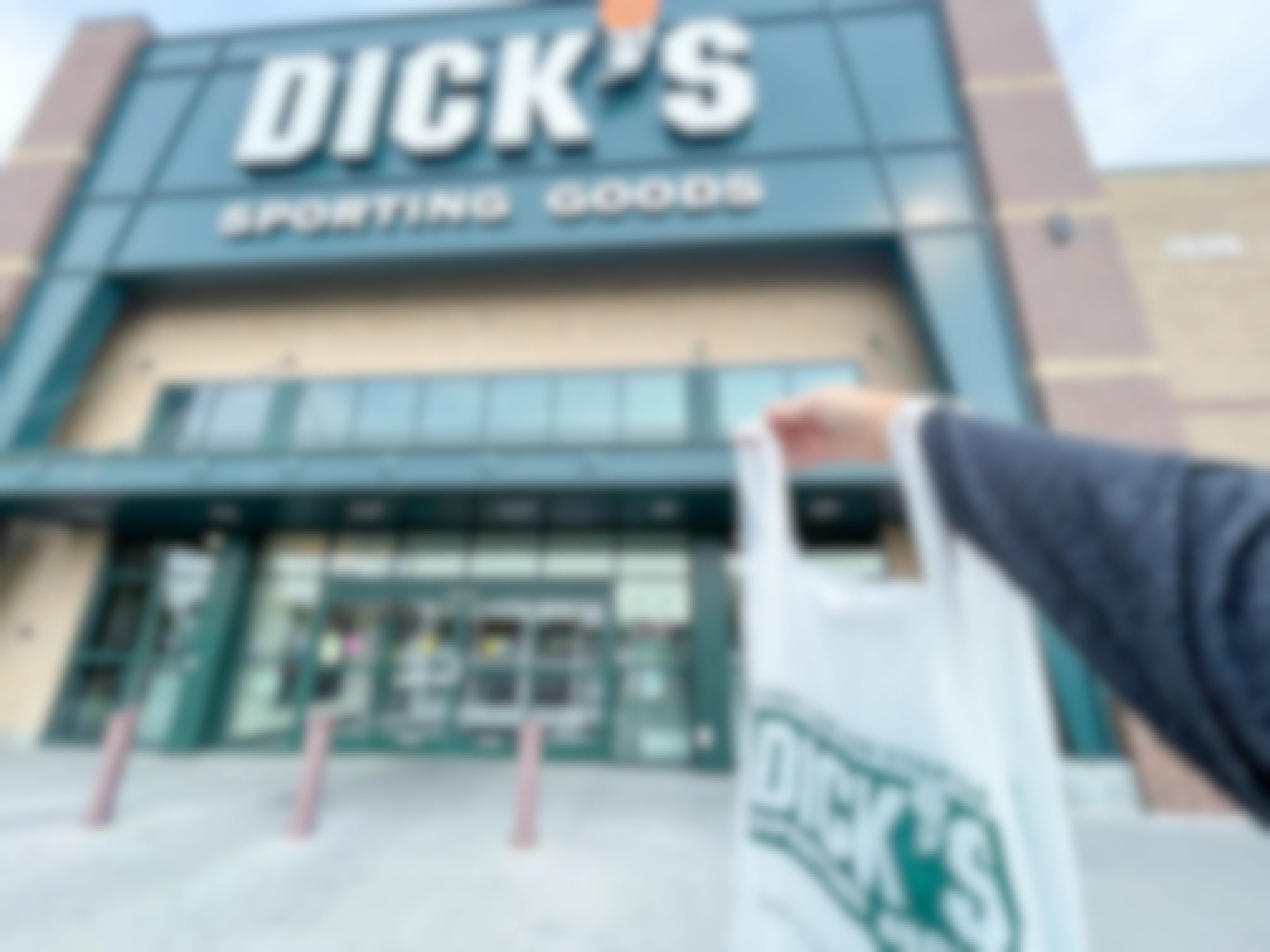 A person holding a shopping bag outside of a Dick's Sporting Goods store front