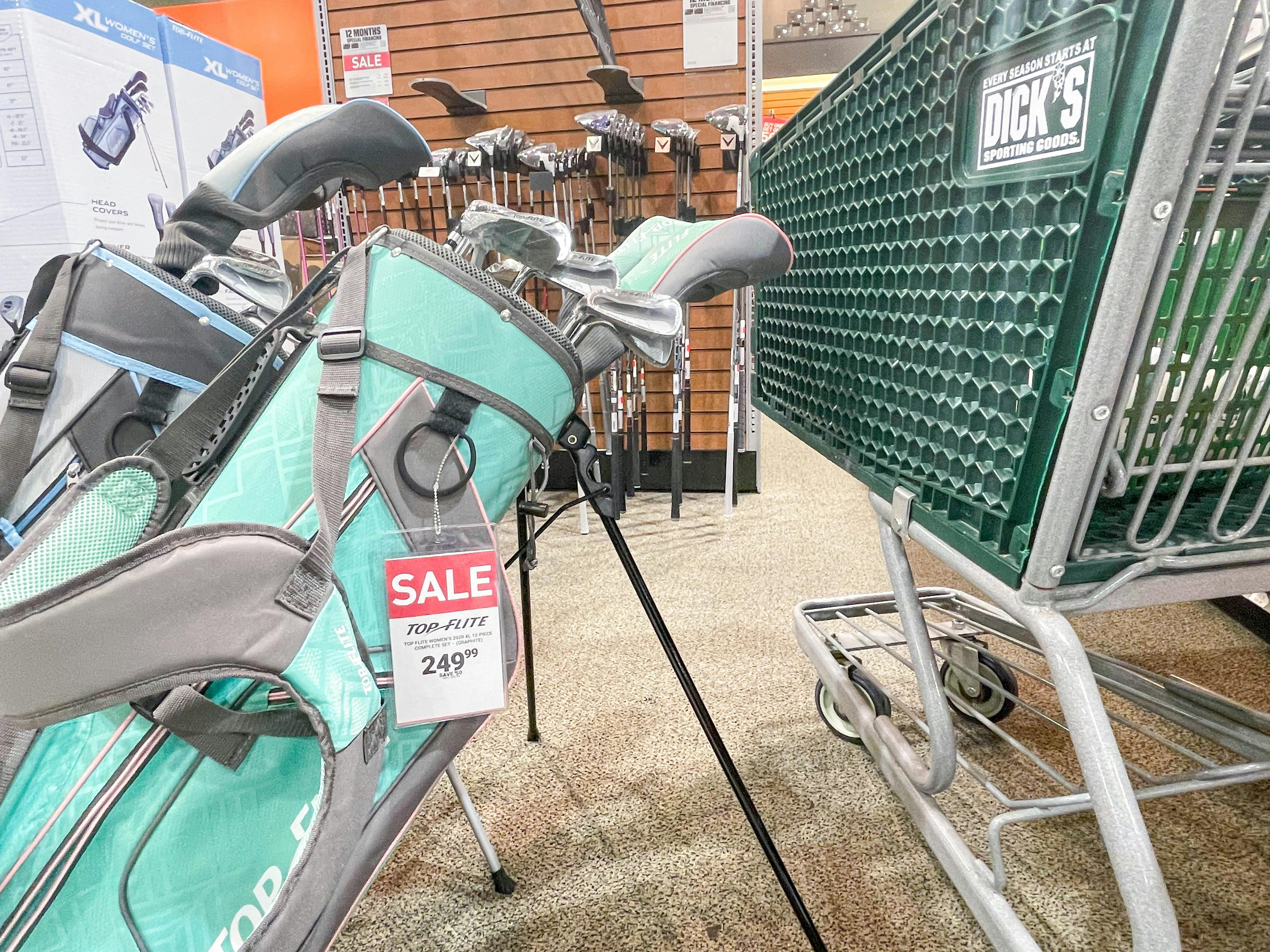 A Dick's Sporting Goods shopping cart parked in front of some Top-Flite golf club sets.