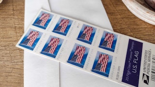 Some USPS American flag Forever postage stamps on top of an envelope on a desk.