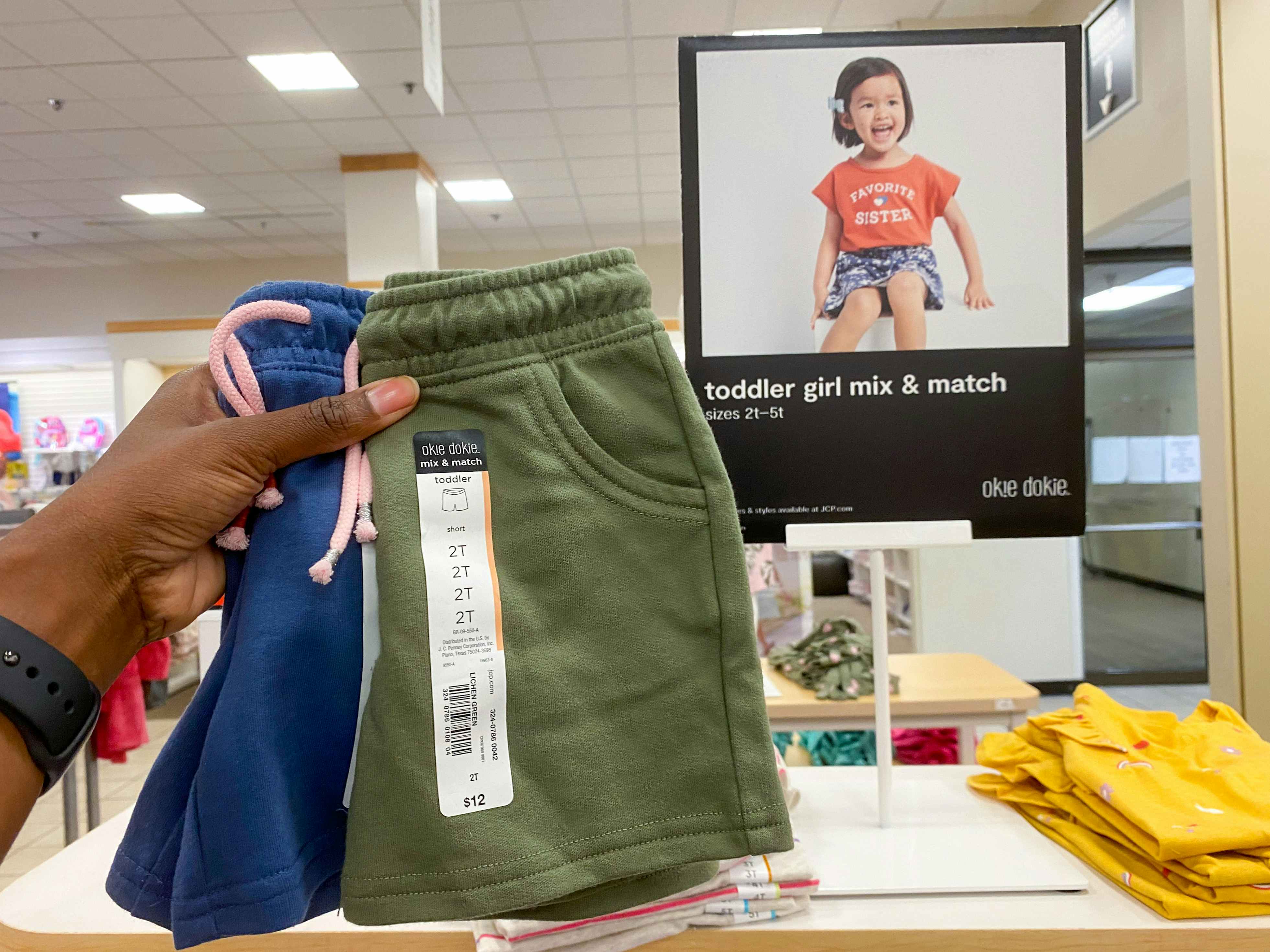 someone holding up two pairs of kids shorts in front of a display sign