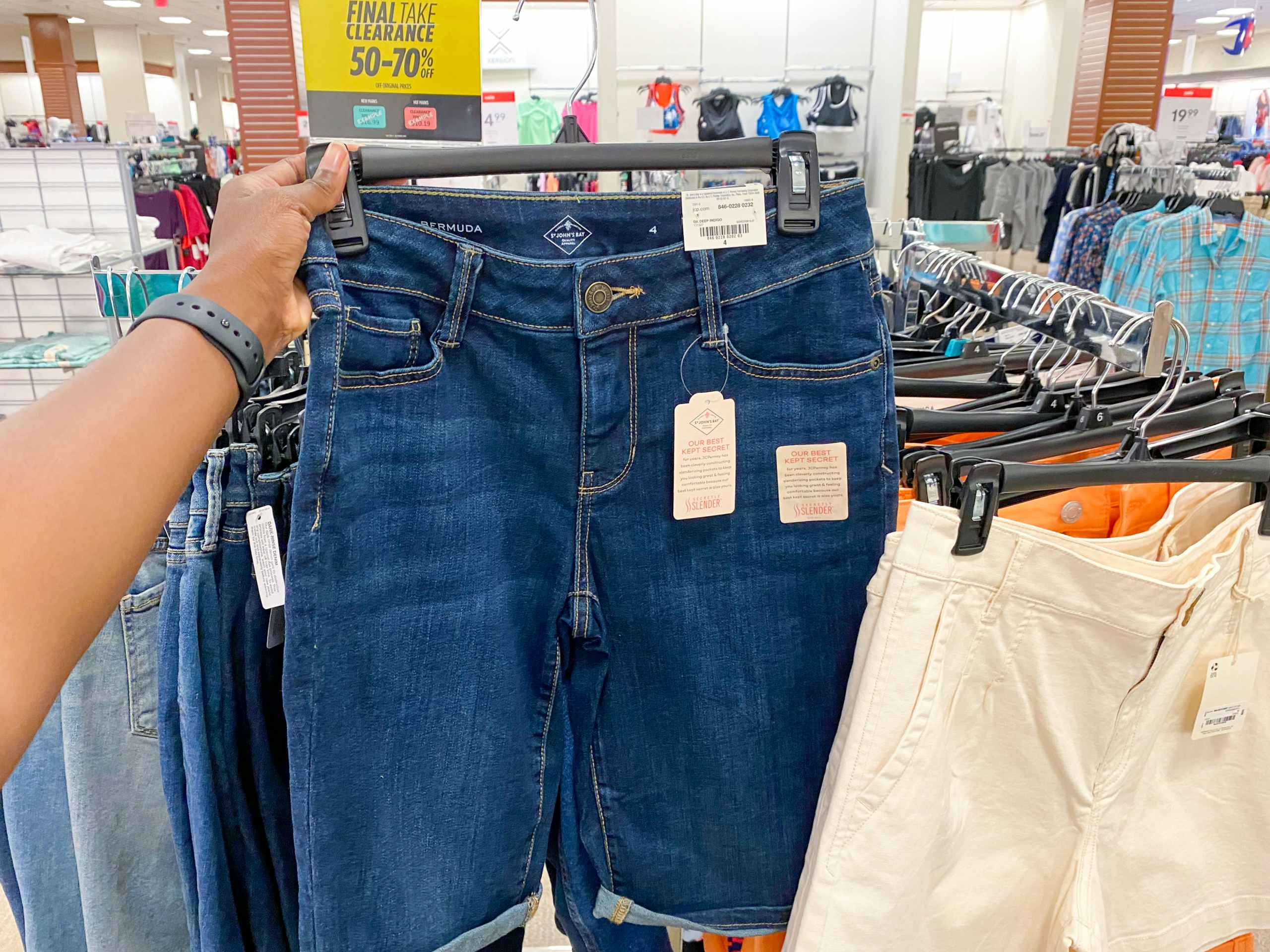 a pair of womens jean shorts held in hand next to racks of shorts in the clearance section in jcpenney