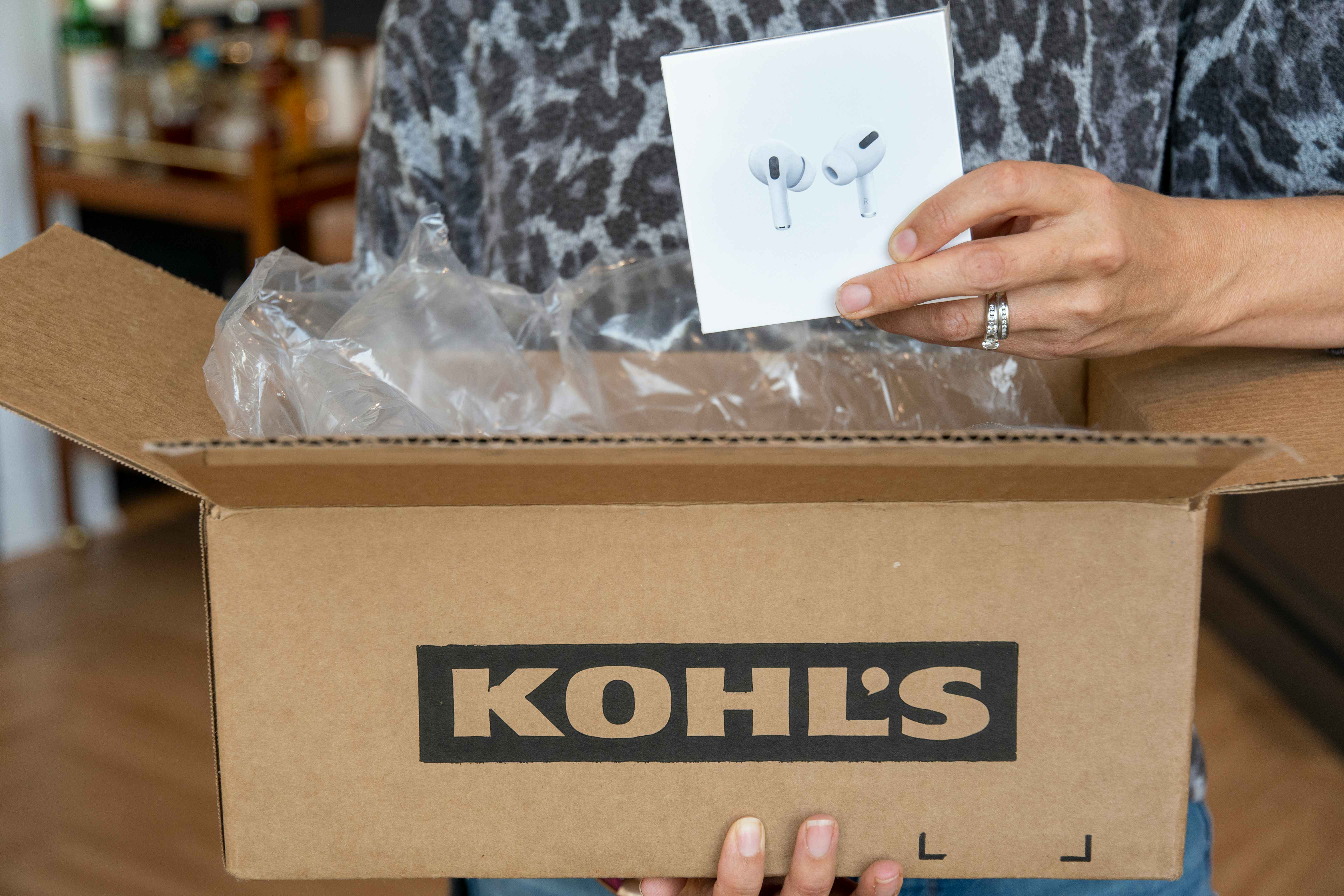 A person taking a pair of Apple Airpods out of a Kohl's box.