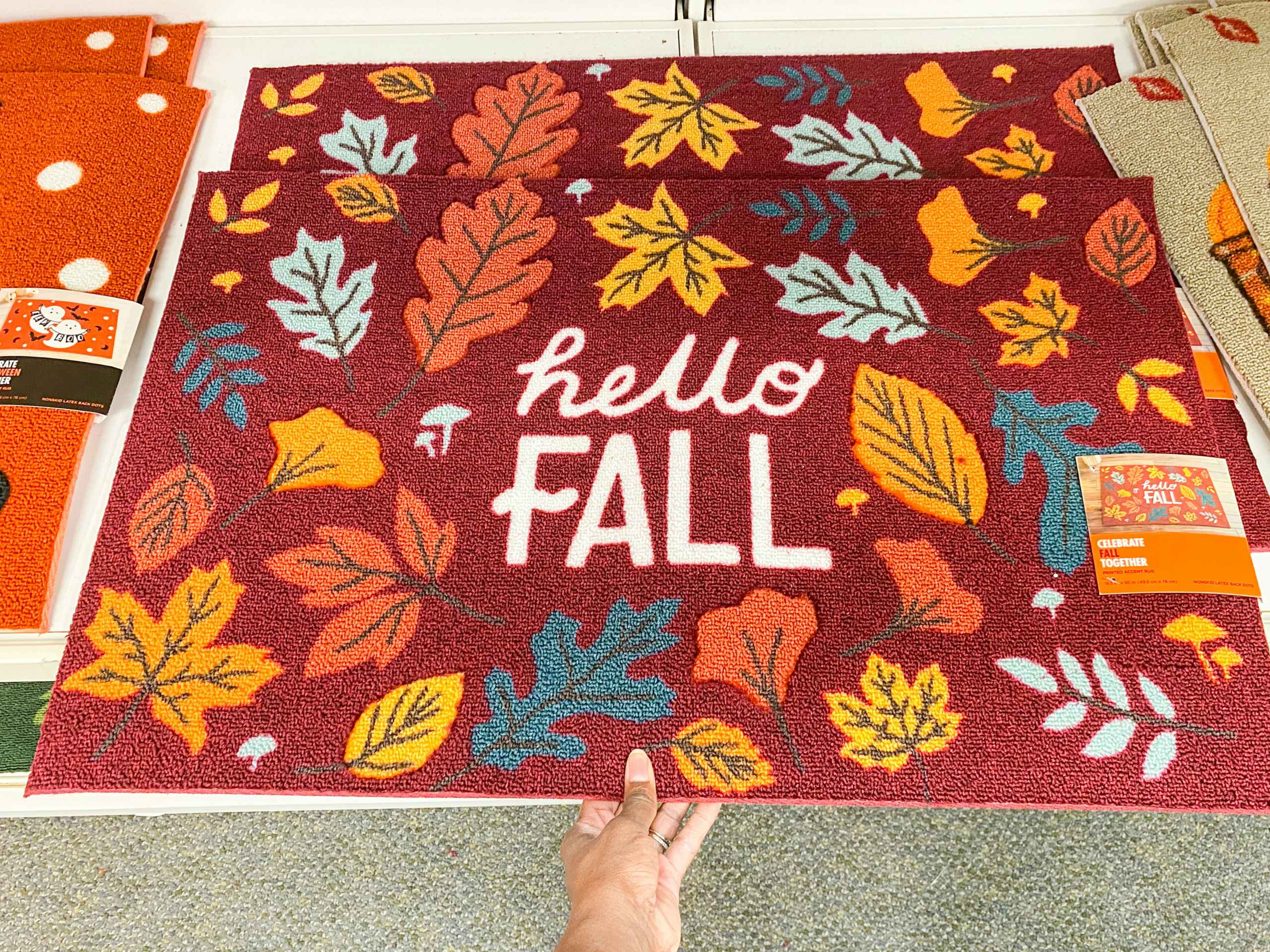 someone pulling put a fall themed entrance rug from a shelf in kohls