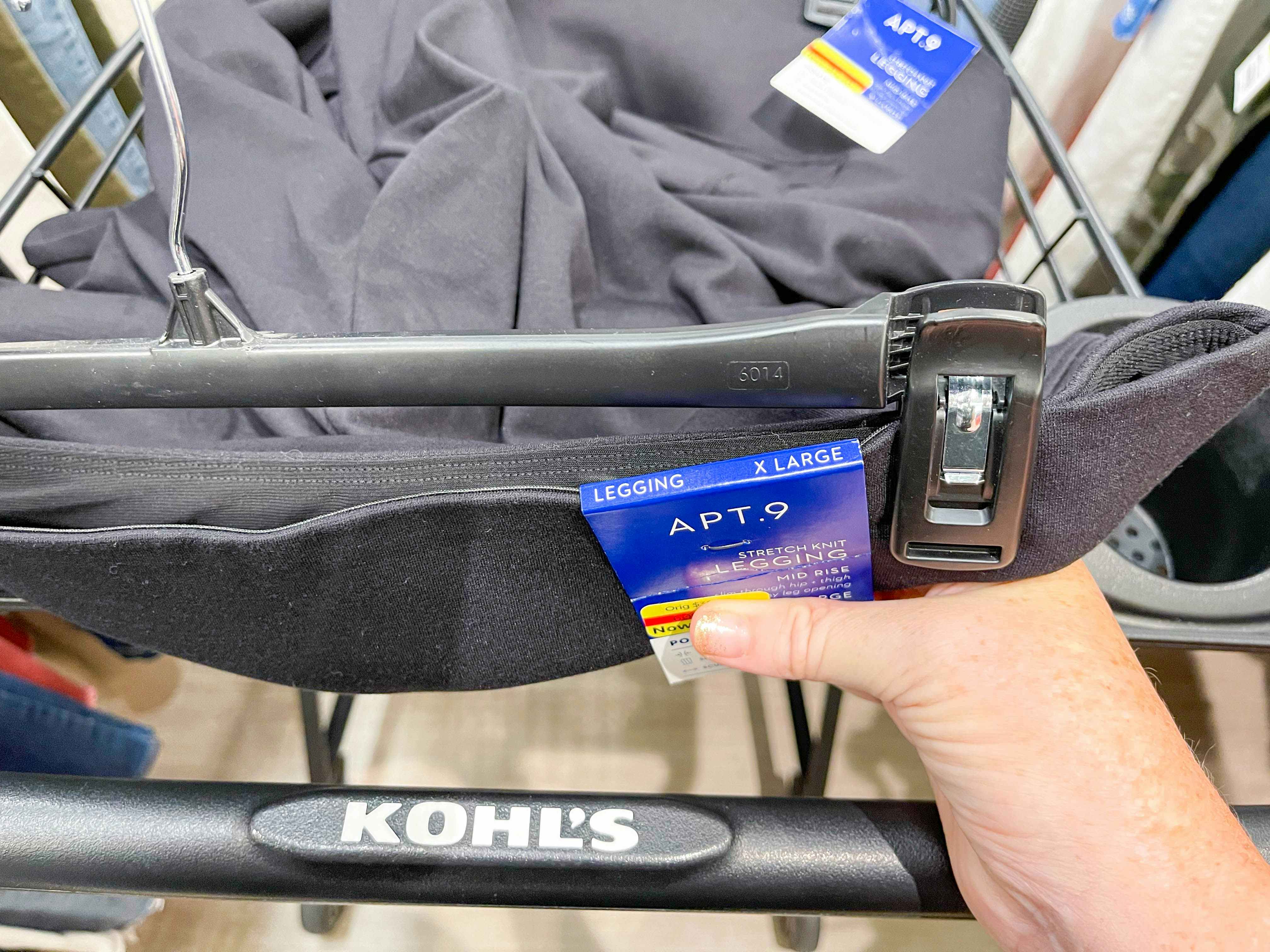 A person putting clearance black leggings into a Kohl's shopping cart.