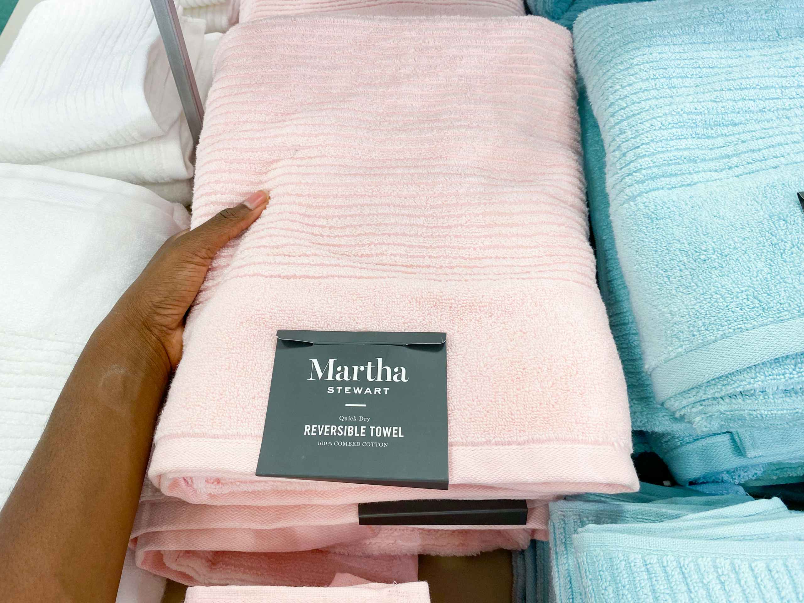 someone picking up a martha Stewart bath towel from a stack of other bath towels on a table in macys'