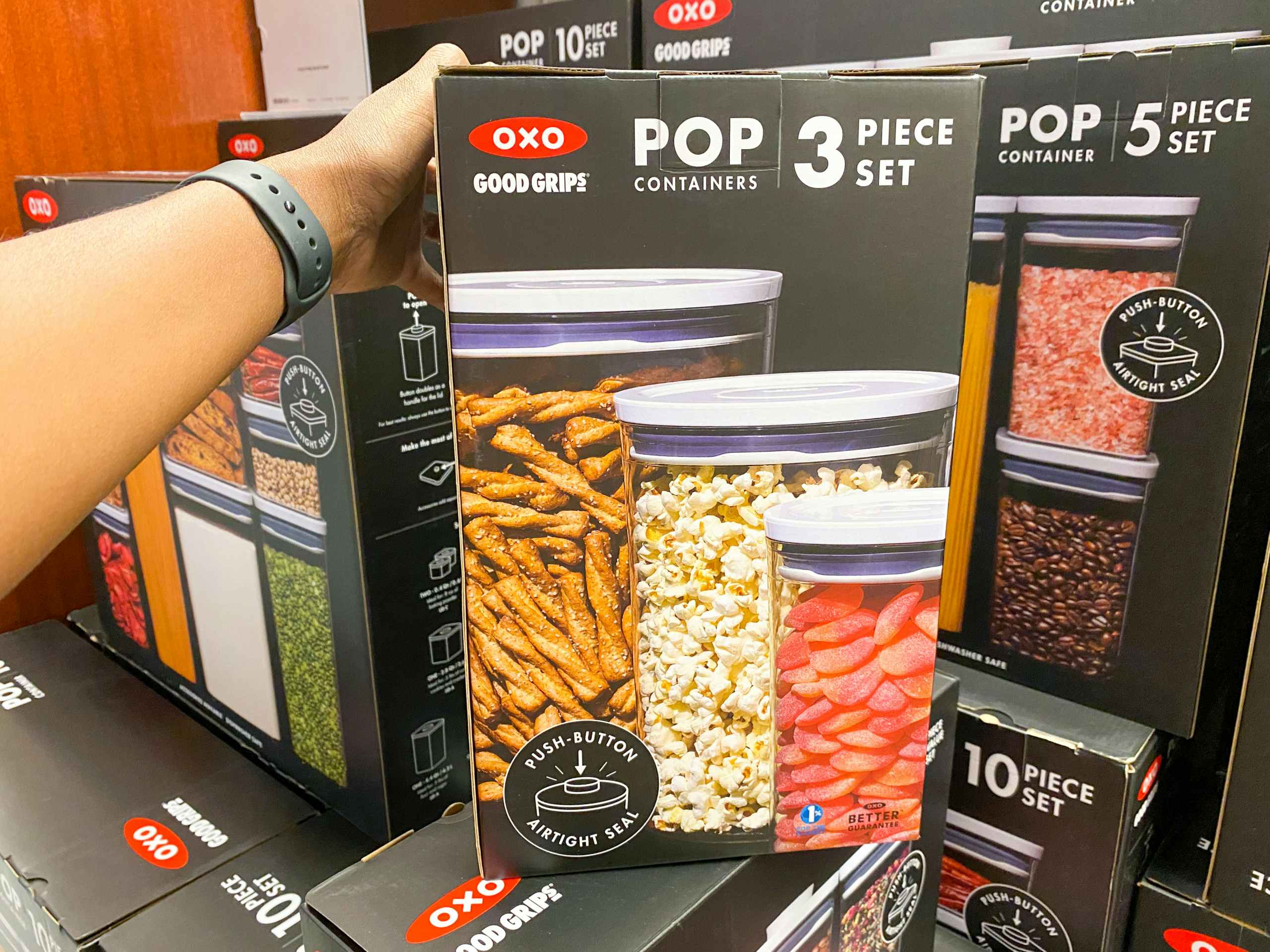 someone grabbing a box of oxo food storage containers on a display of other containers in macys