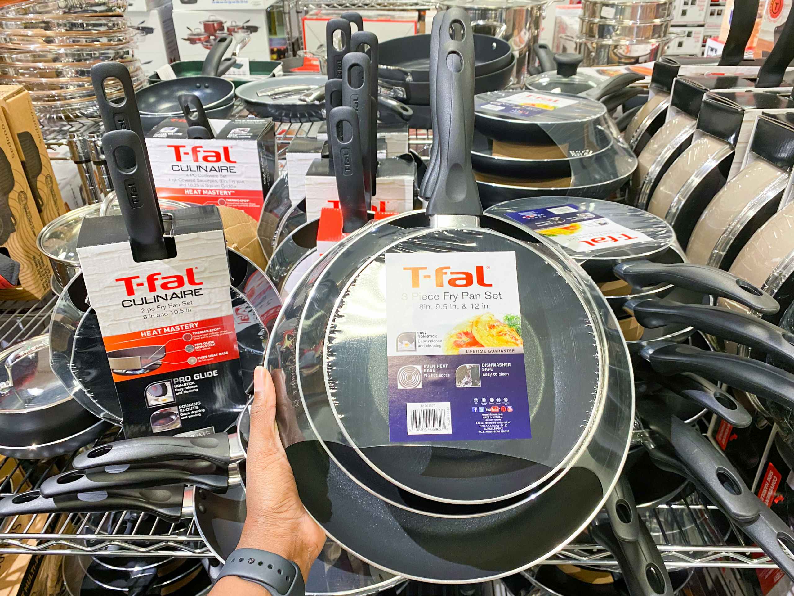 a t-fal frying pan set held up in front of a display of other pan sets in macys