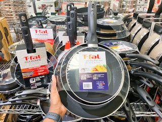 a t-fal frying pan set held up in front of a display of other pan sets in macys