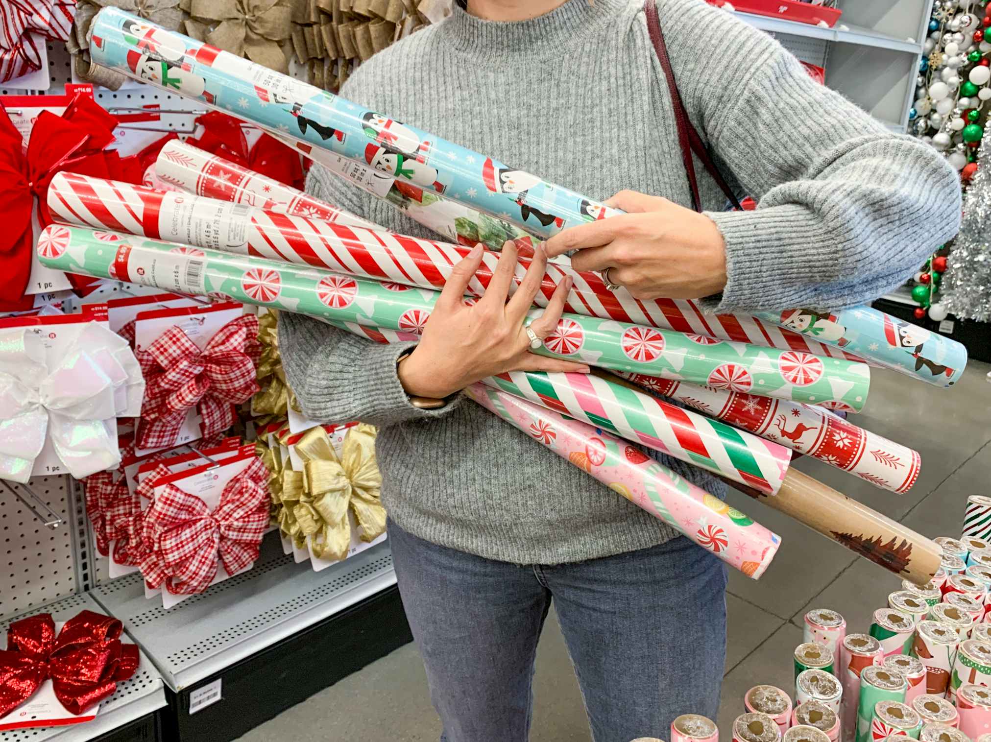 A woman holding an arm full of Christmas gift wrap