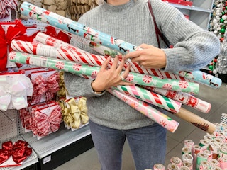 A woman holding an arm full of Christmas gift wrap