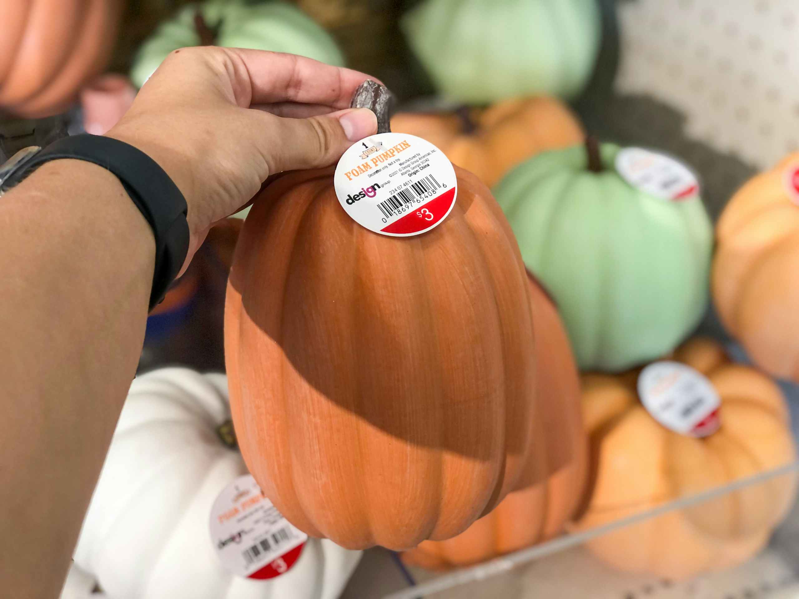 hand holding out small fake pumokin in front of pumpkin display at Target