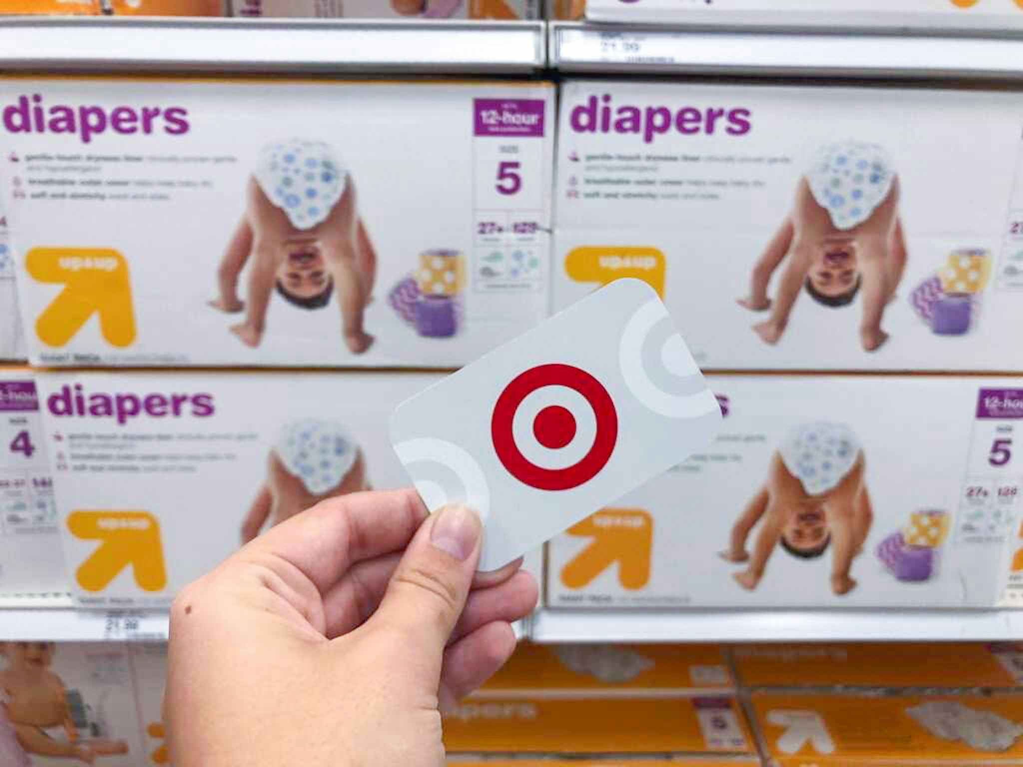hand holding a target gift card in front of up & up diapers