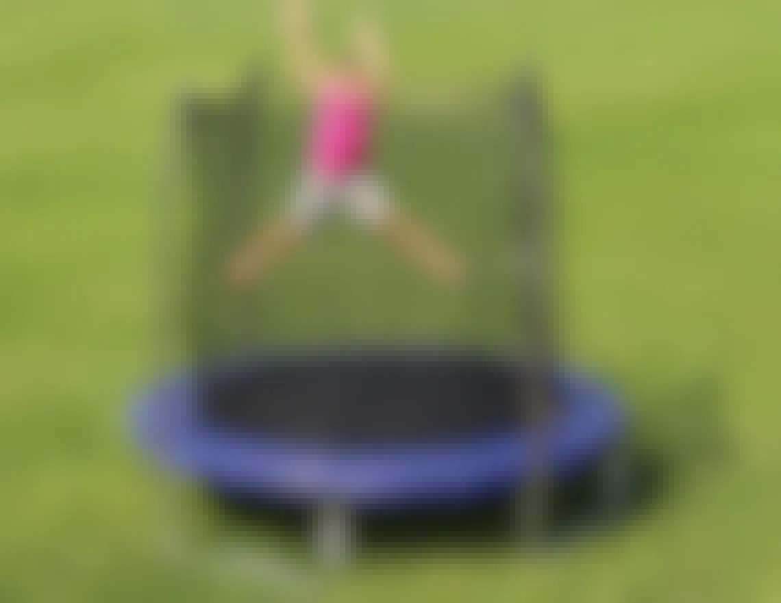 A little girl jumping on a Skywalker Trampolines 8' Trampoline with Safety Enclosure in a backyard