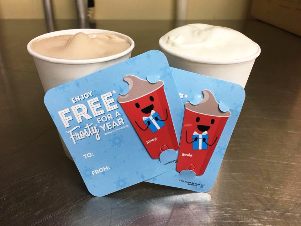 Two Wendy's "Enjoy Free Frosty for a yearr" keychain cards in front of a chocolate and vanilla frosty on a table at Wendy's.