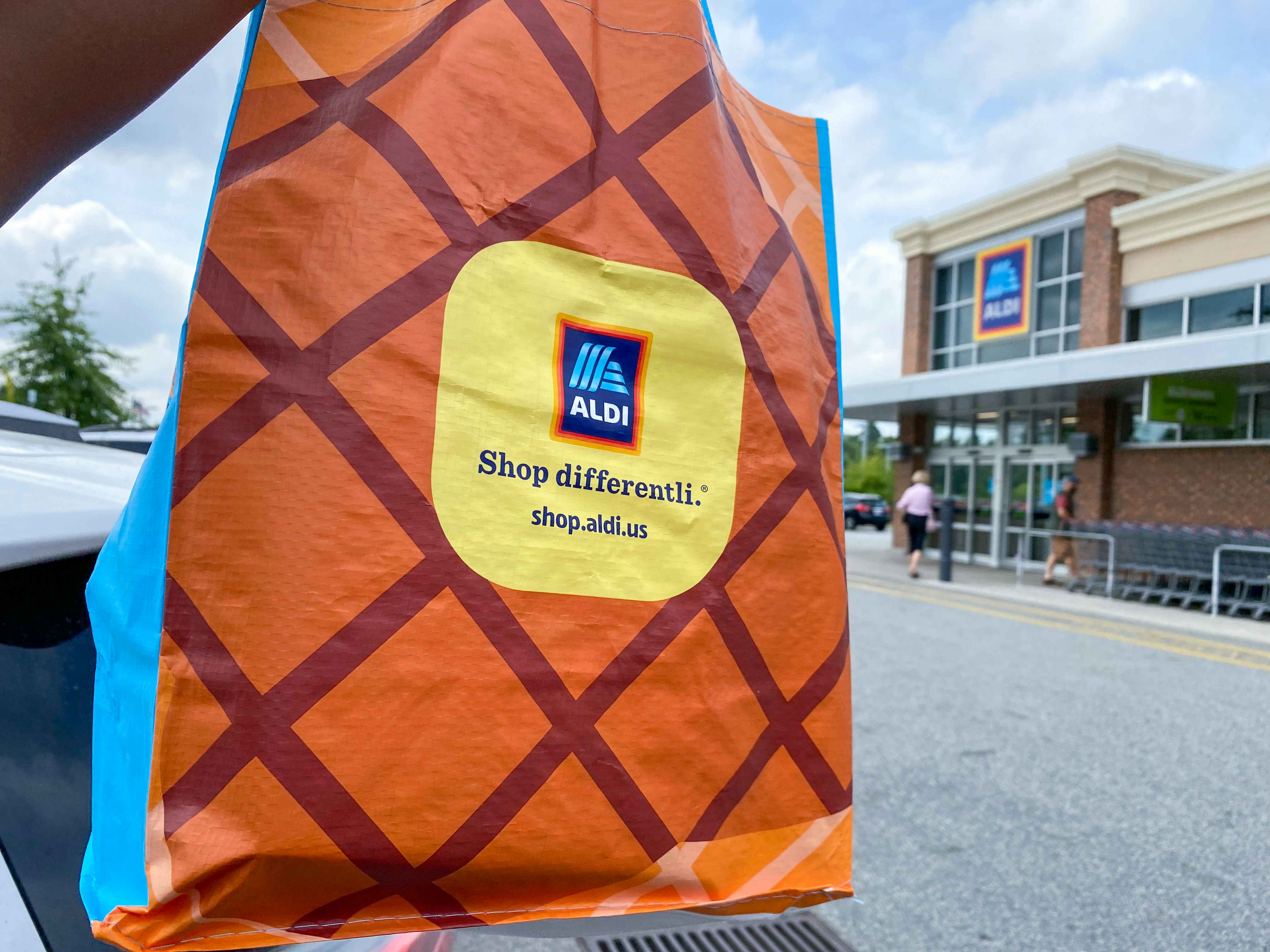 an Aldi reusable bag being held up in front of an Aldi store