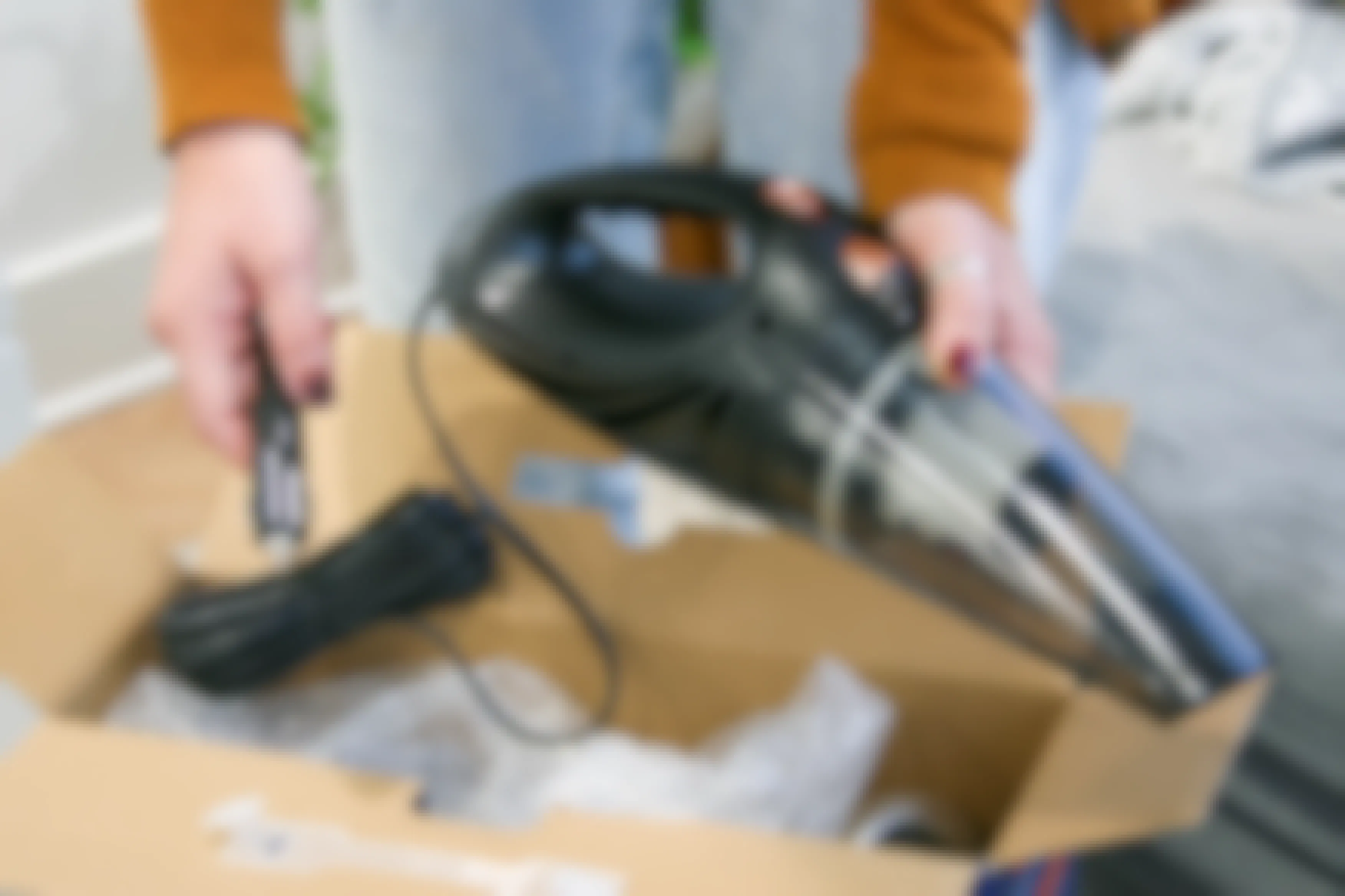 A person taking a corded car vacuum out of a box.