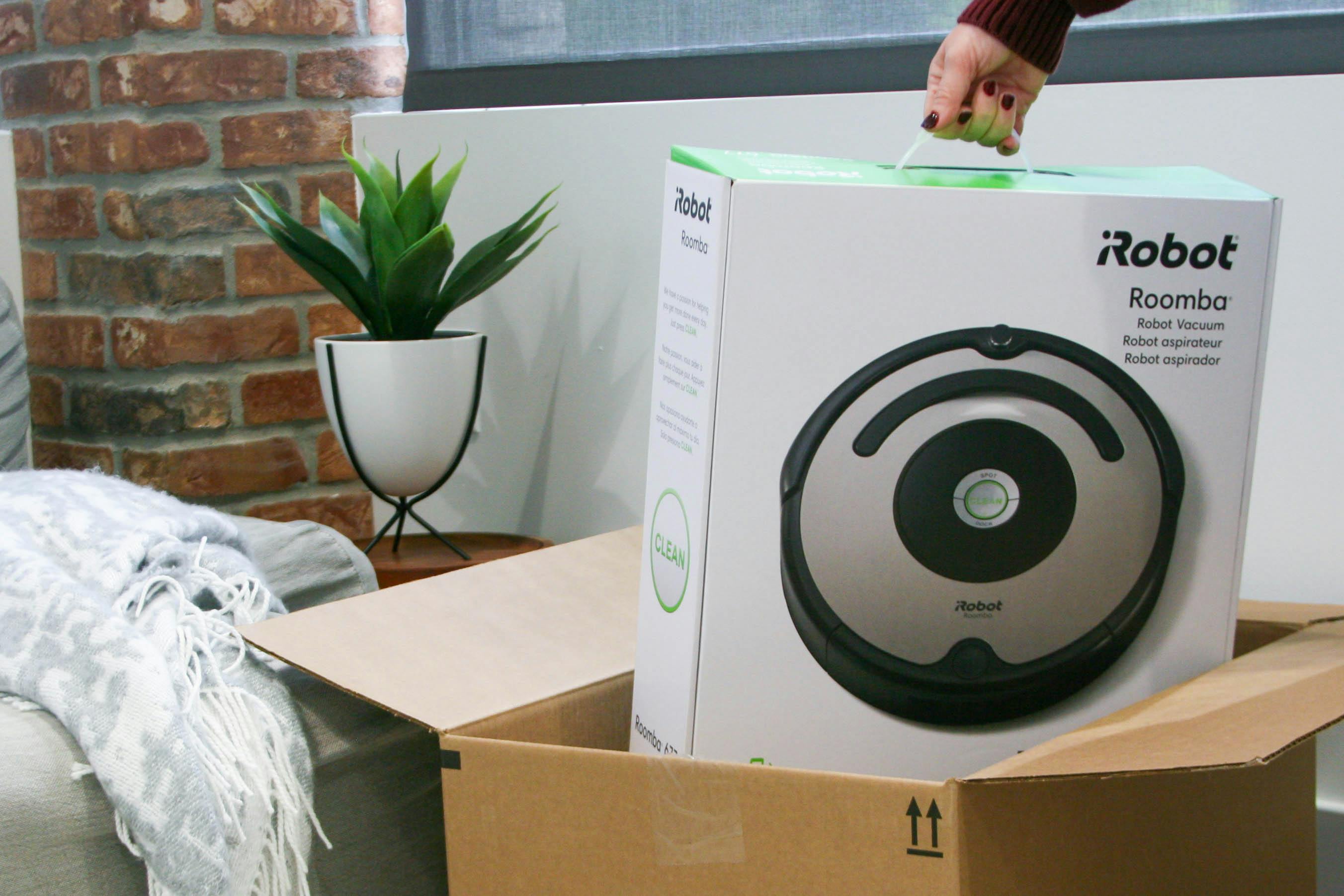A person's hand lifting an iRobot Roomba out of a box.