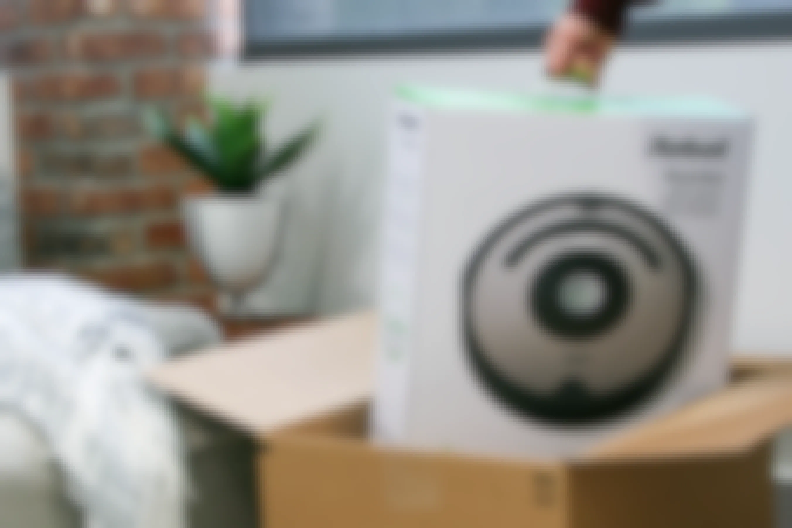 A person's hand lifting an iRobot Roomba out of a box.