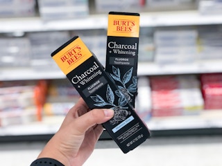 hand holding two boxes of Burt's Bees toothpaste in front of toothpaste aisle at Target