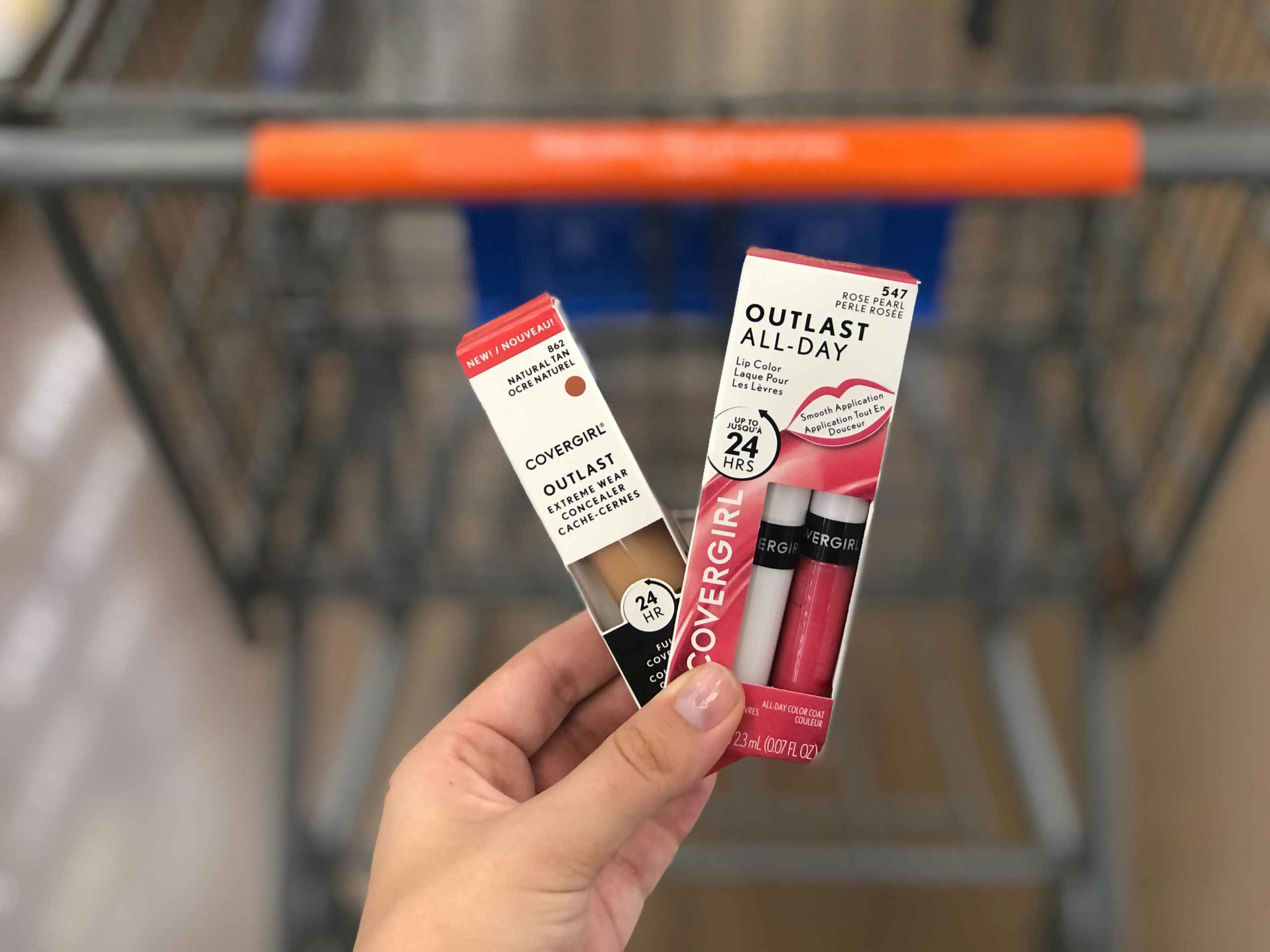 hand holding two Covergirl cosmetics items in front of store cart