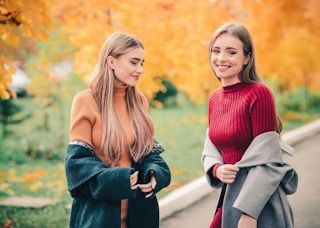 Two smiling women wearing sweaters outside in autumn.