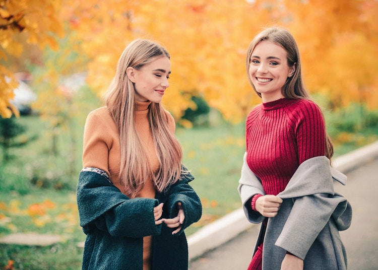 Two smiling women wearing sweaters outside in autumn.