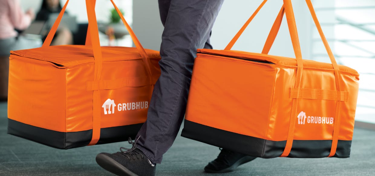 A low angle view of a person walking and carrying two large Grubhub meal delivery bags.