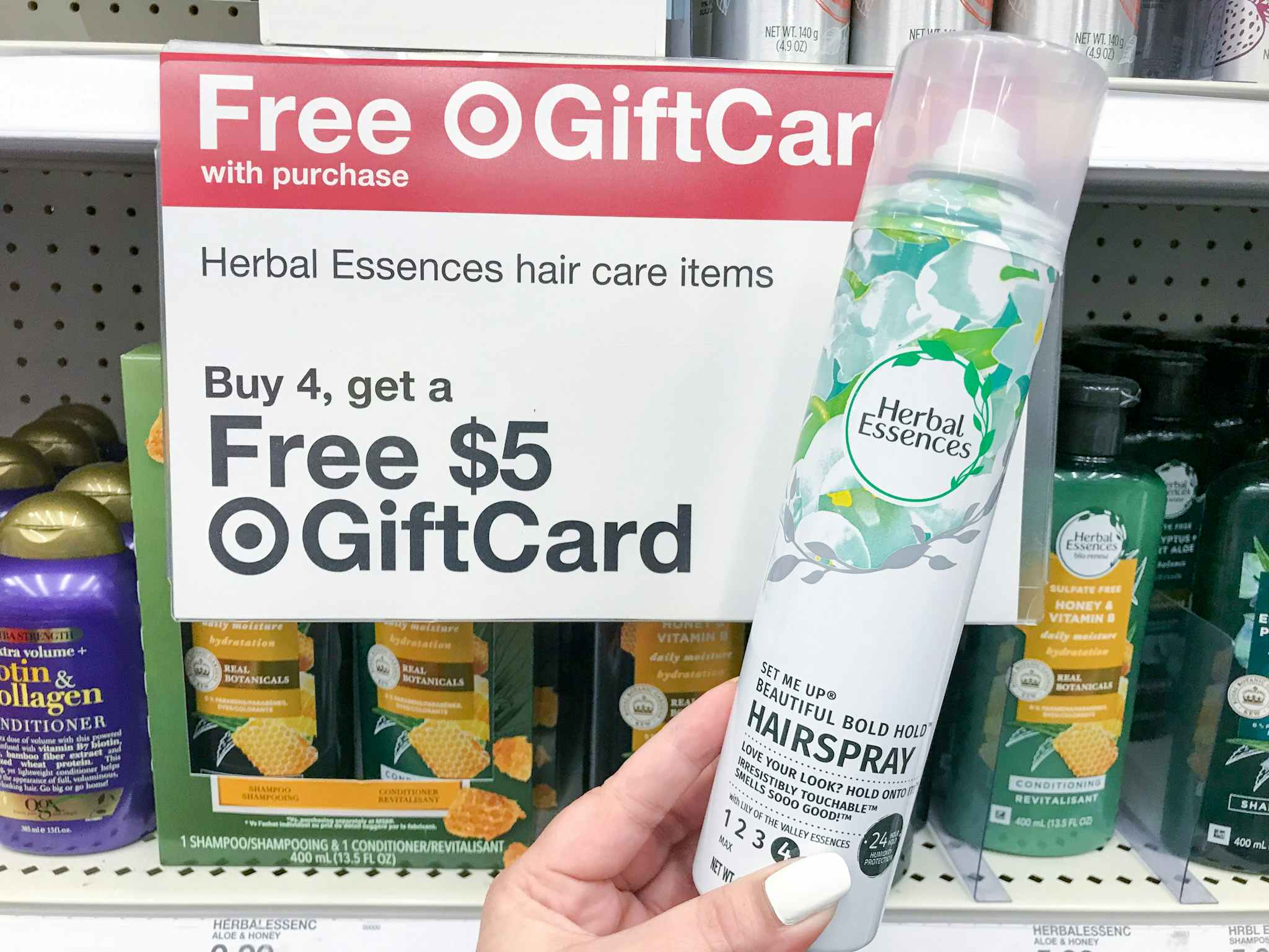 hand holding a herbal essences hairspray in front of a target gift card promotion sign