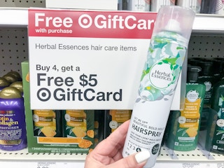 hand holding a herbal essences hairspray in front of a target gift card promotion sign