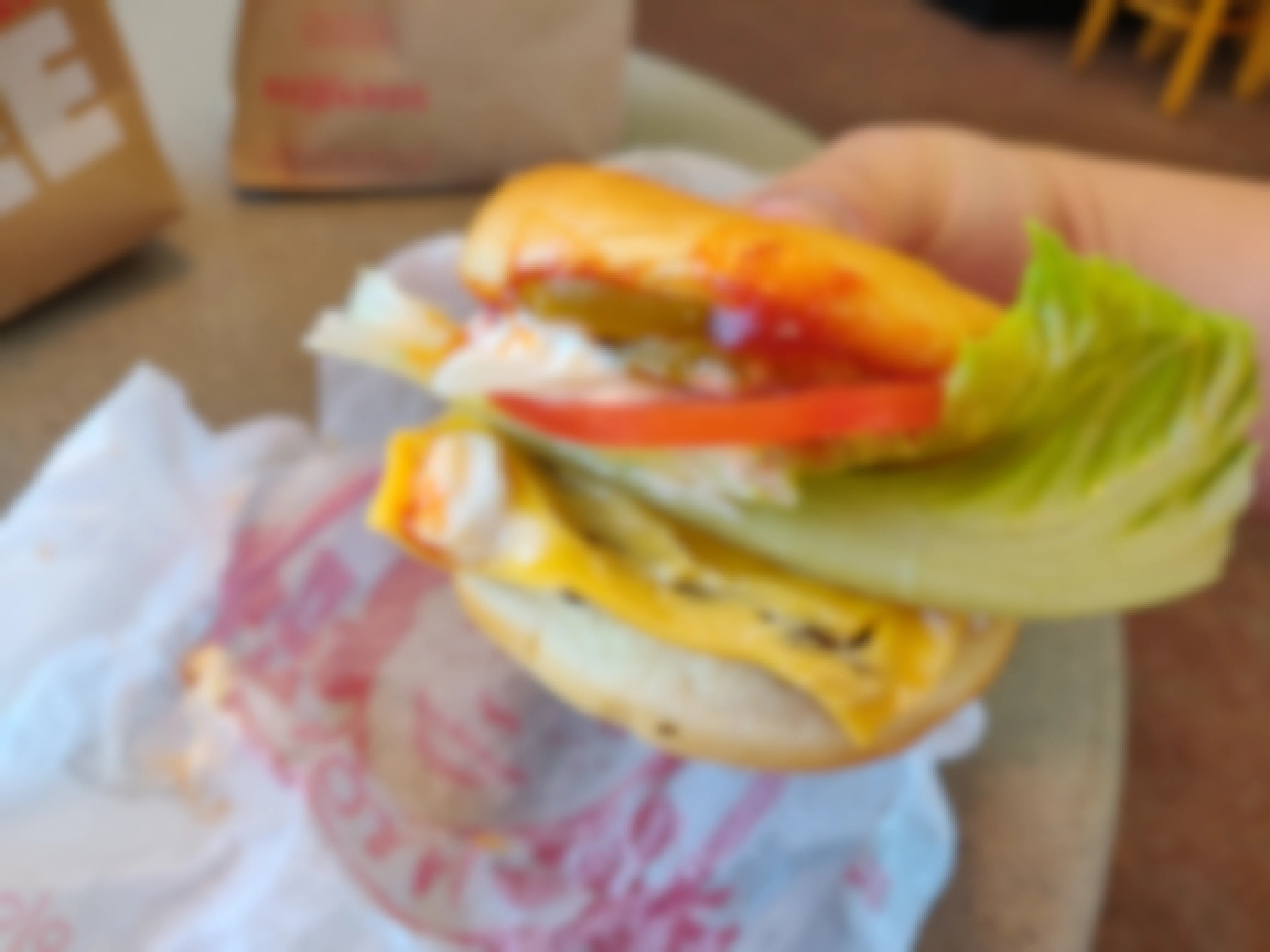 A person's hand holding a Wendy's Jr. Cheeseburger with extra lettuce and tomatoes.
