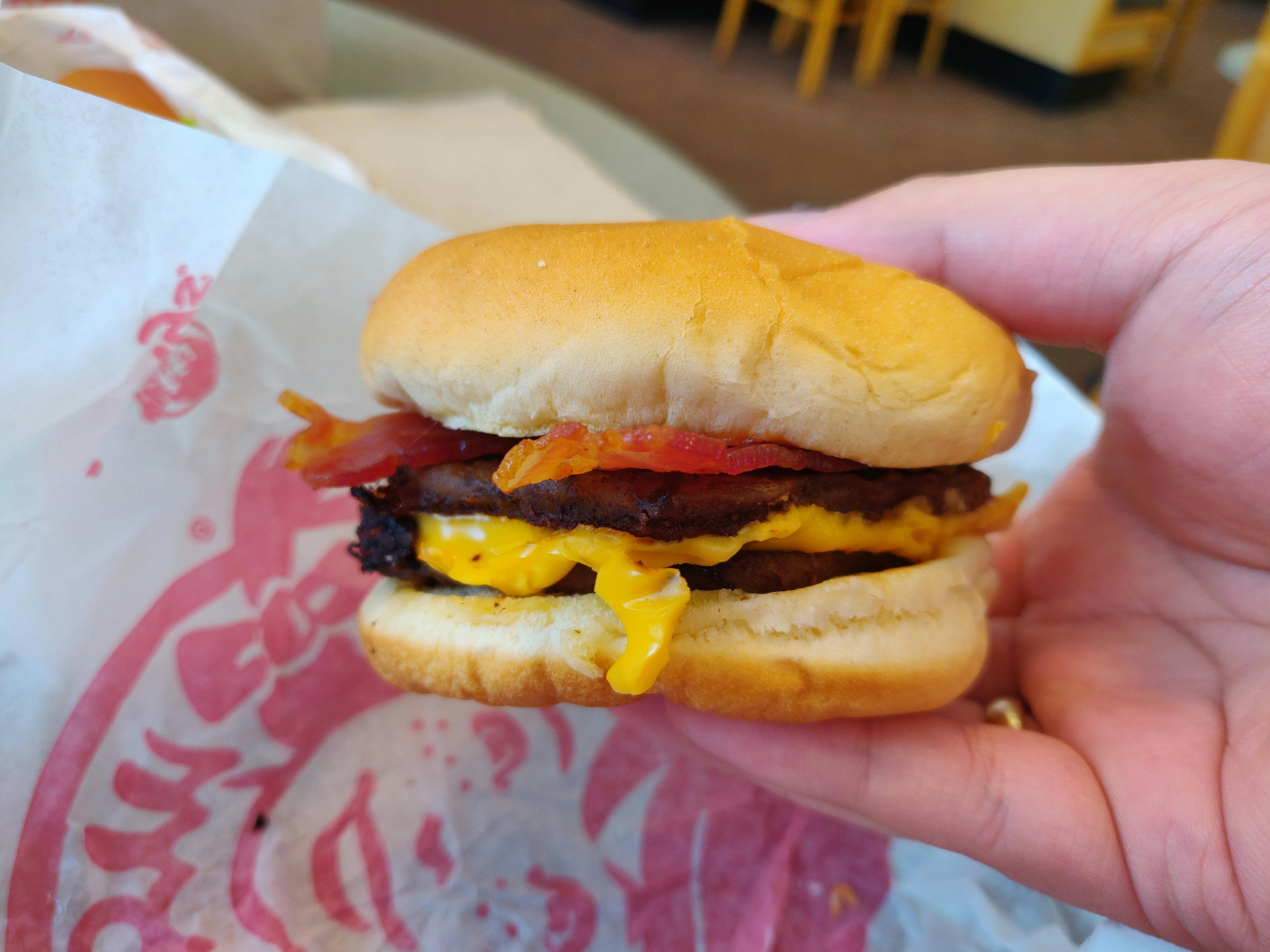 A person's hand holding a Wendy's Bacon Double Stack burger above its paper wrapper..