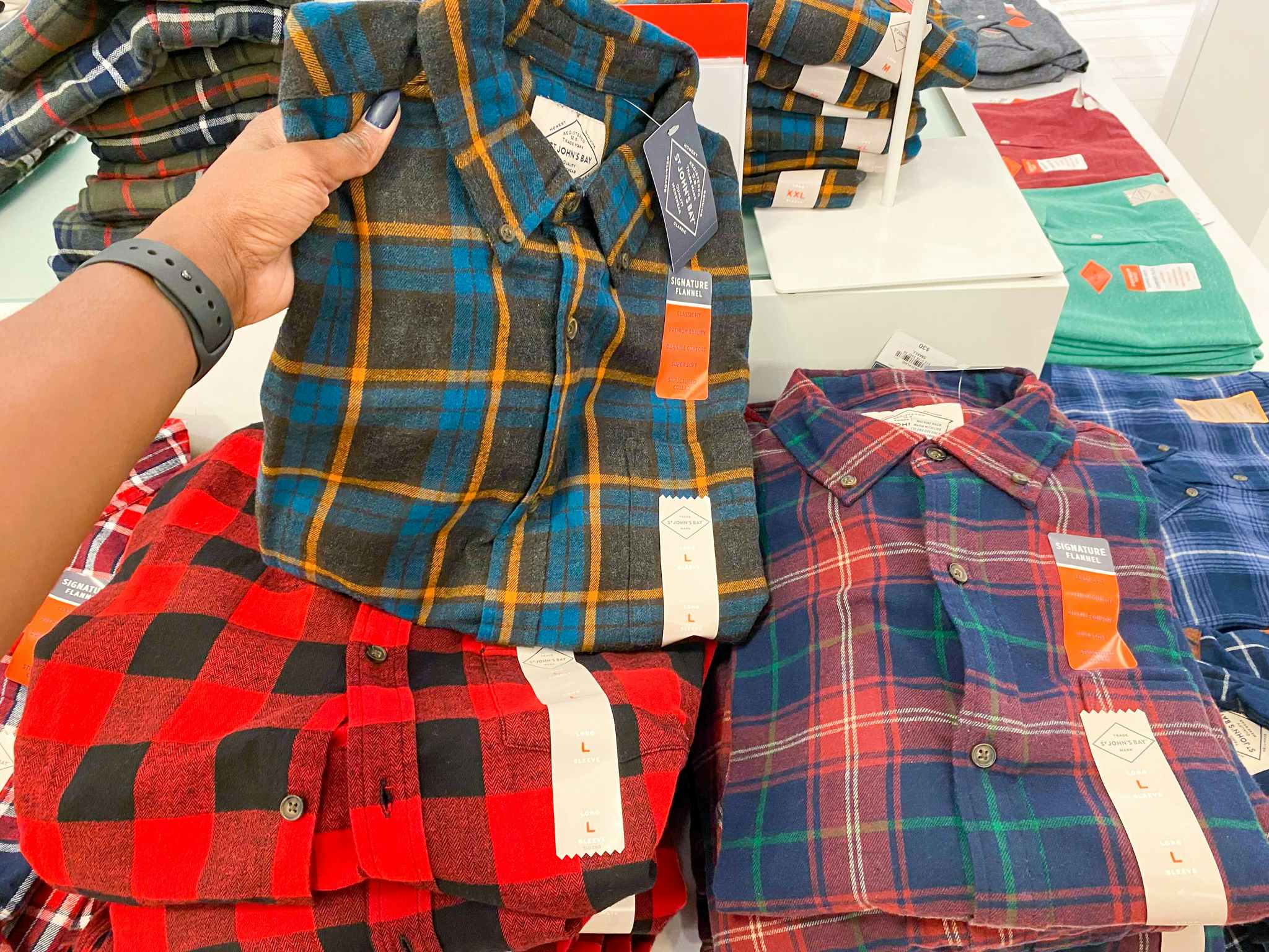 hand holding men's flannel shirt in front of display