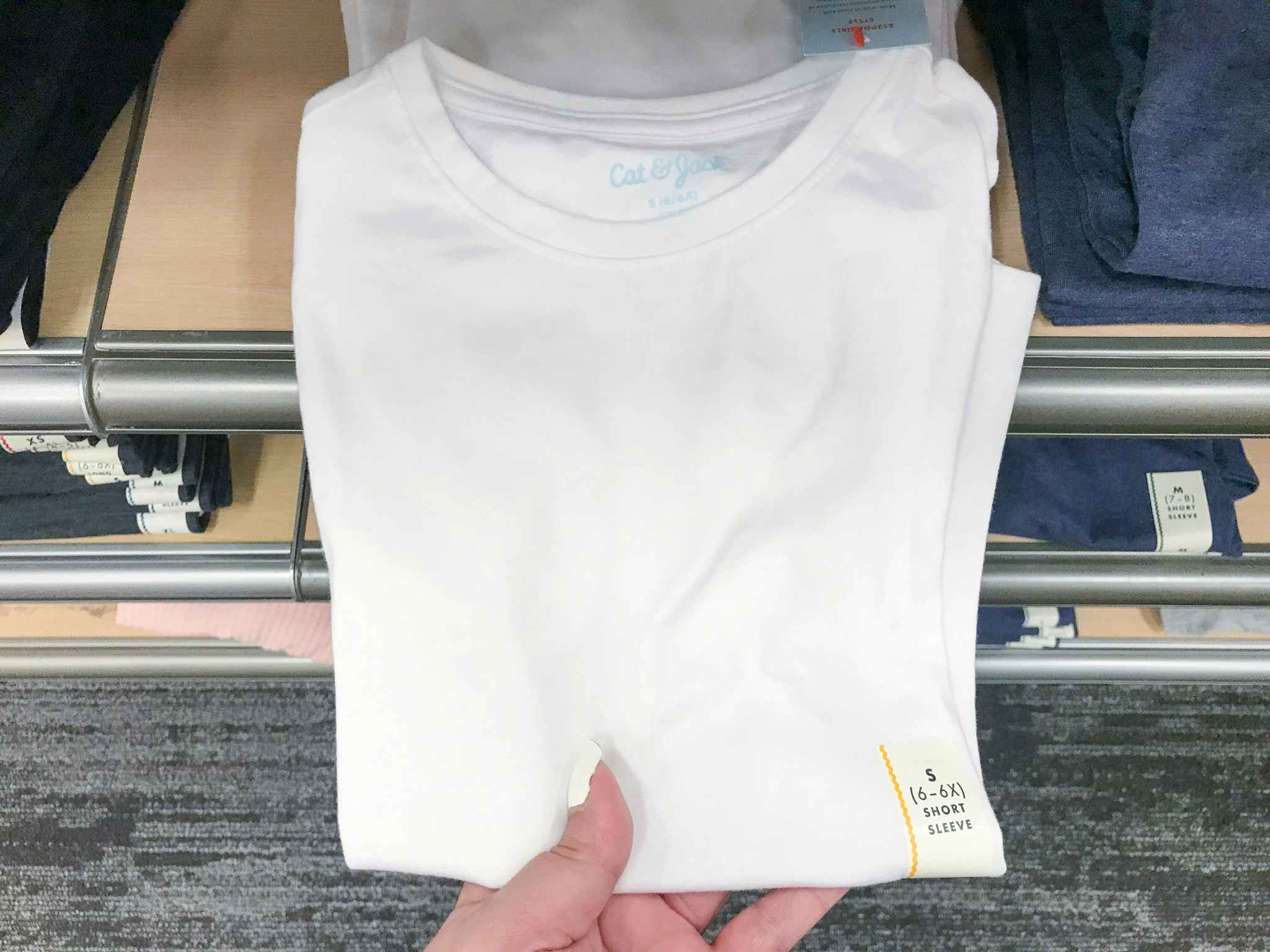 hand grabbing a white cat & jack t-shirt off a target shelf