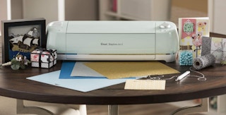 A mint Cricut Explore Air 2 on a table near crafting materials.