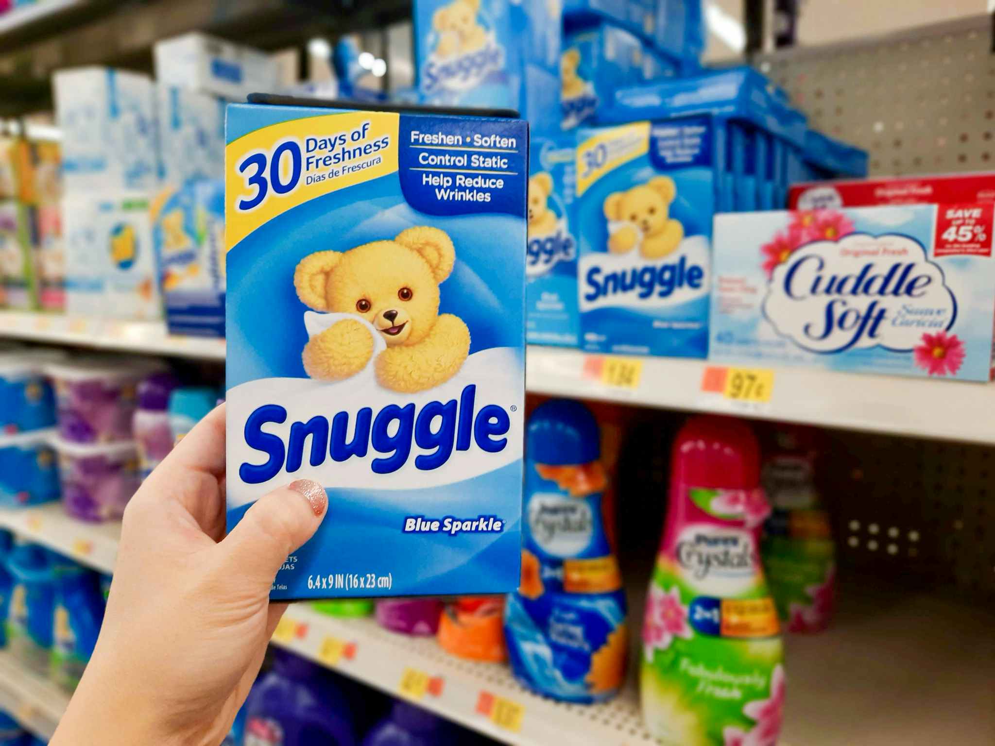hand holding out box of Snuggle dryer sheets in front of Walmart store shelf