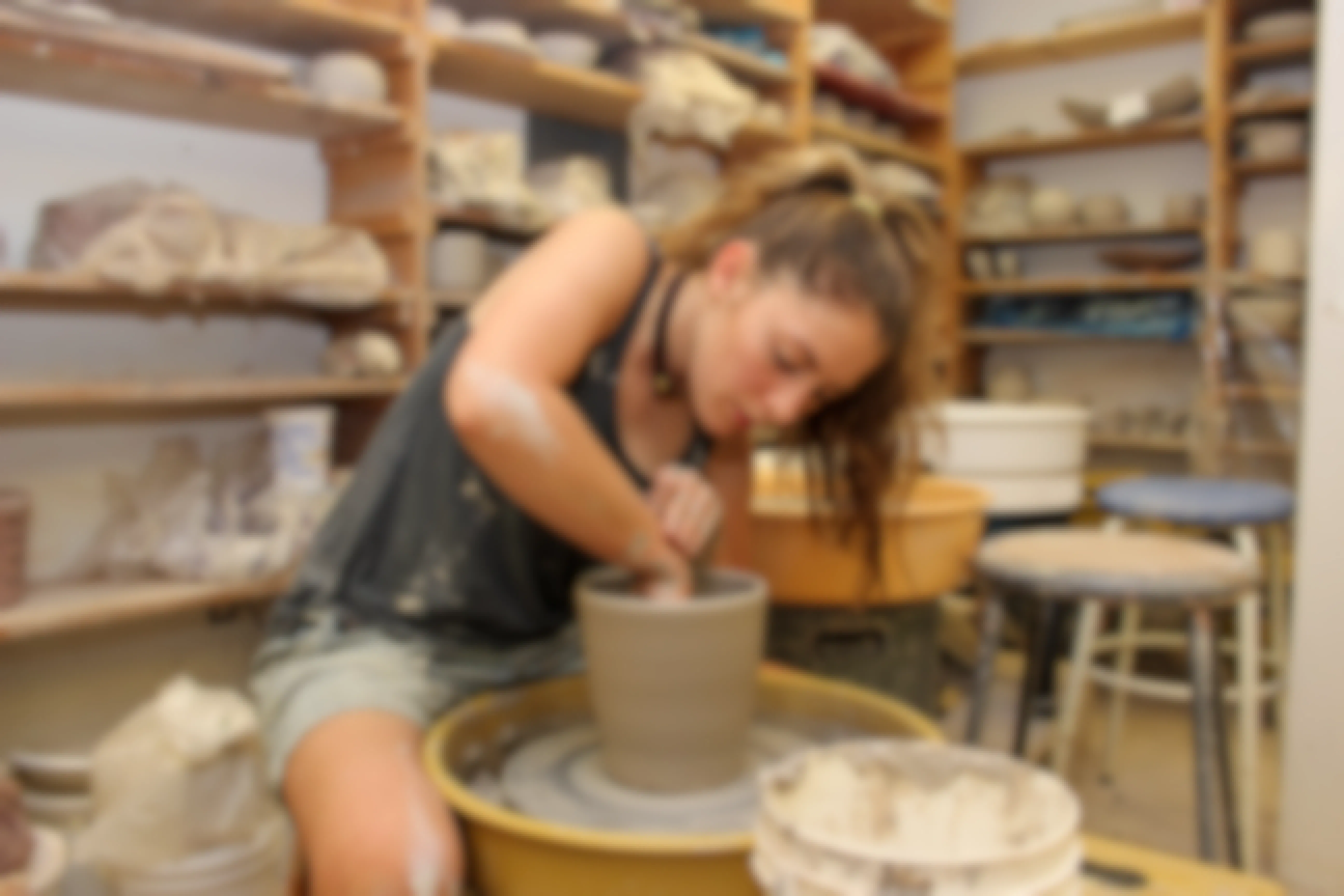 A teen girl making a pot on a pottery wheel.