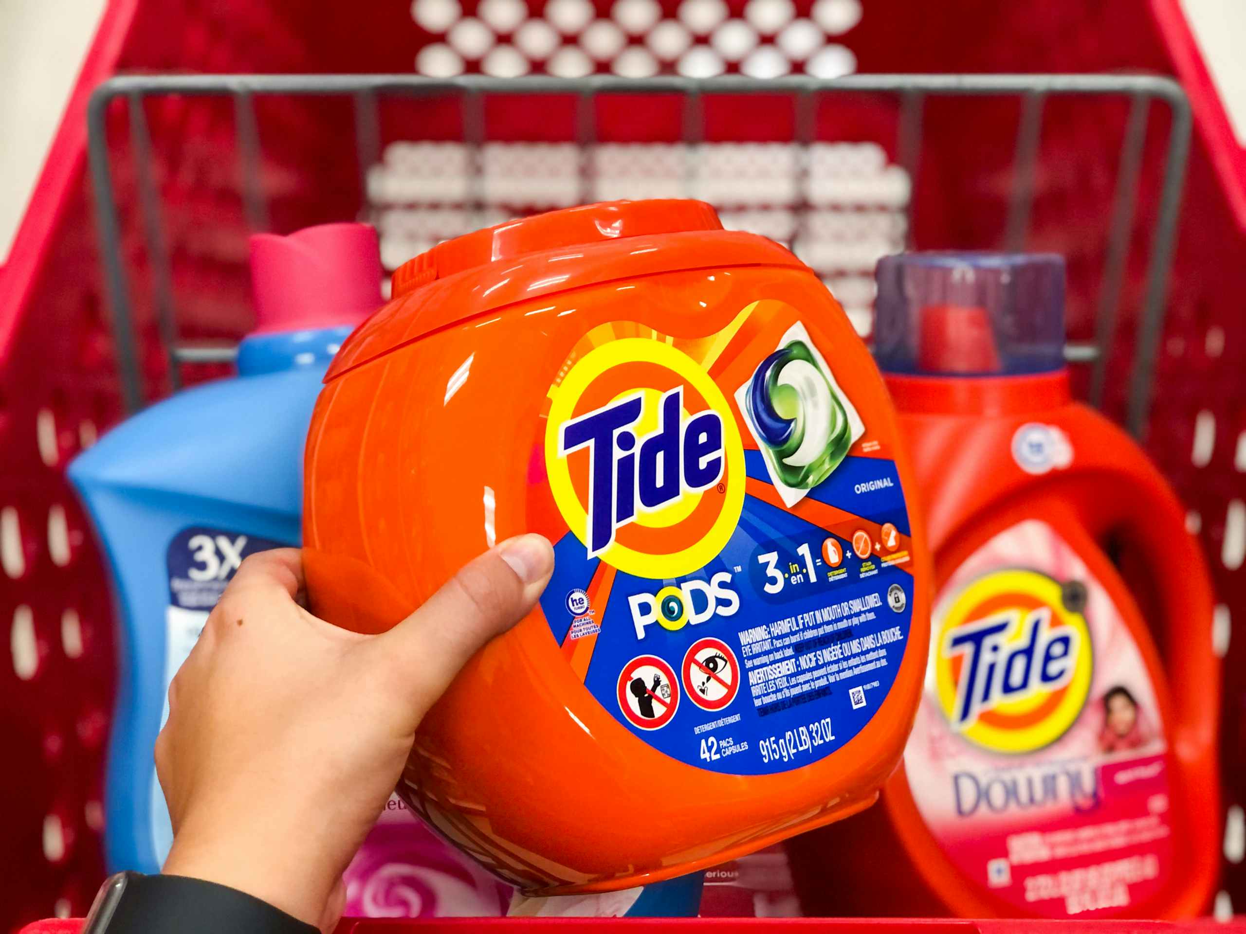 hand holding tide pods in front of store shopping cart