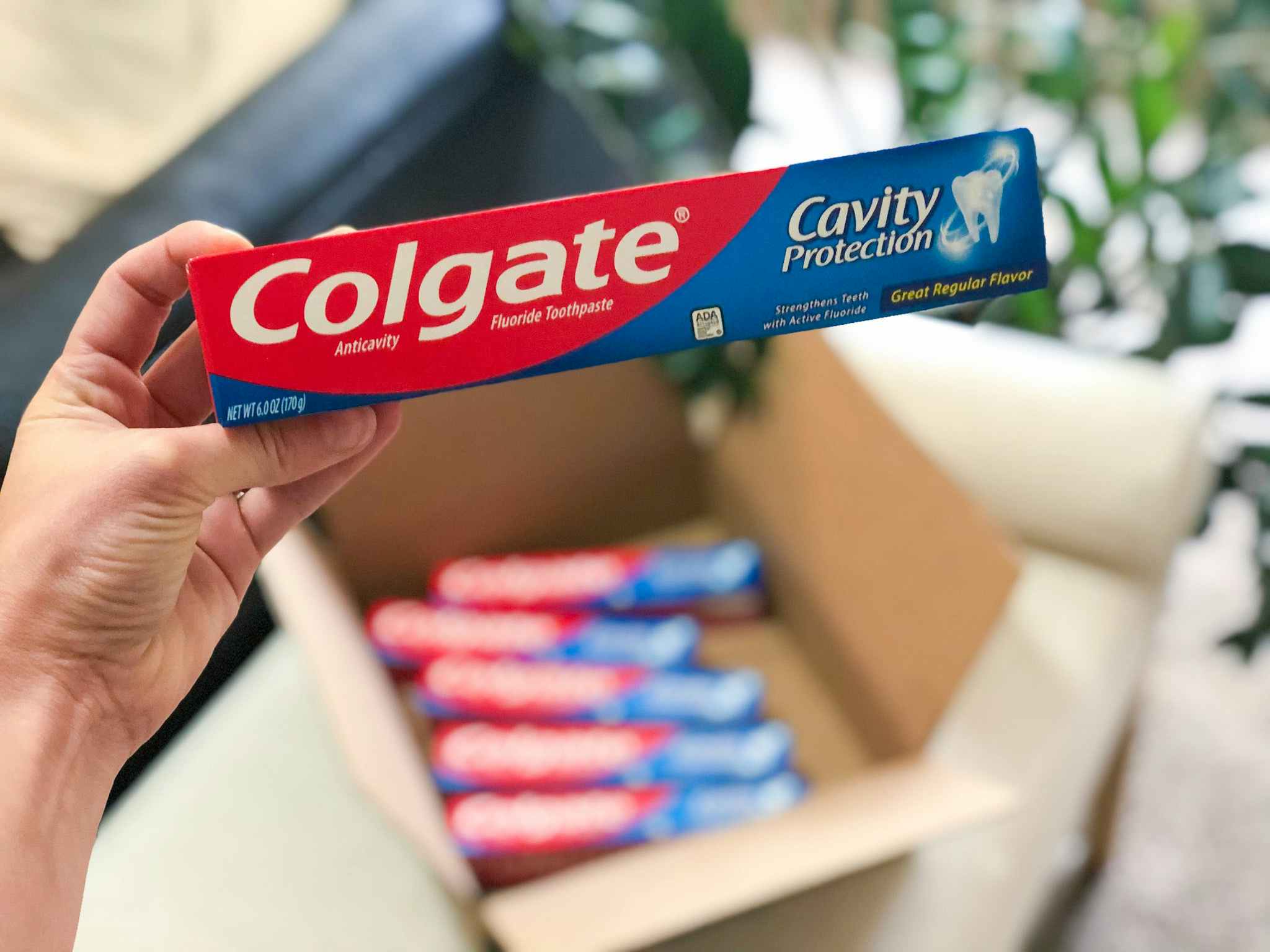person holding colgate cavity protection toothpaste near box