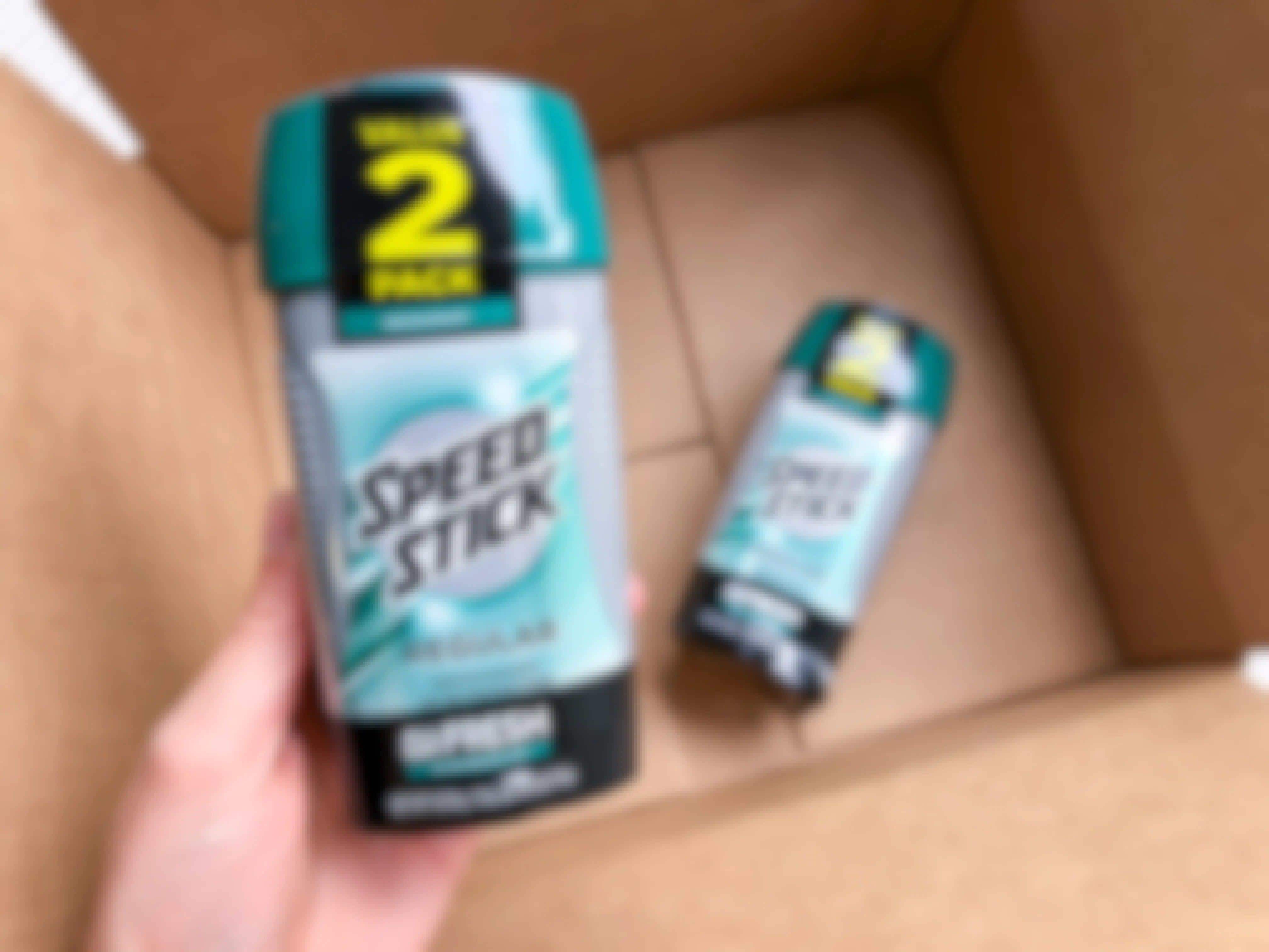 A hand holding Speed Stick deodrant over a delivery box.