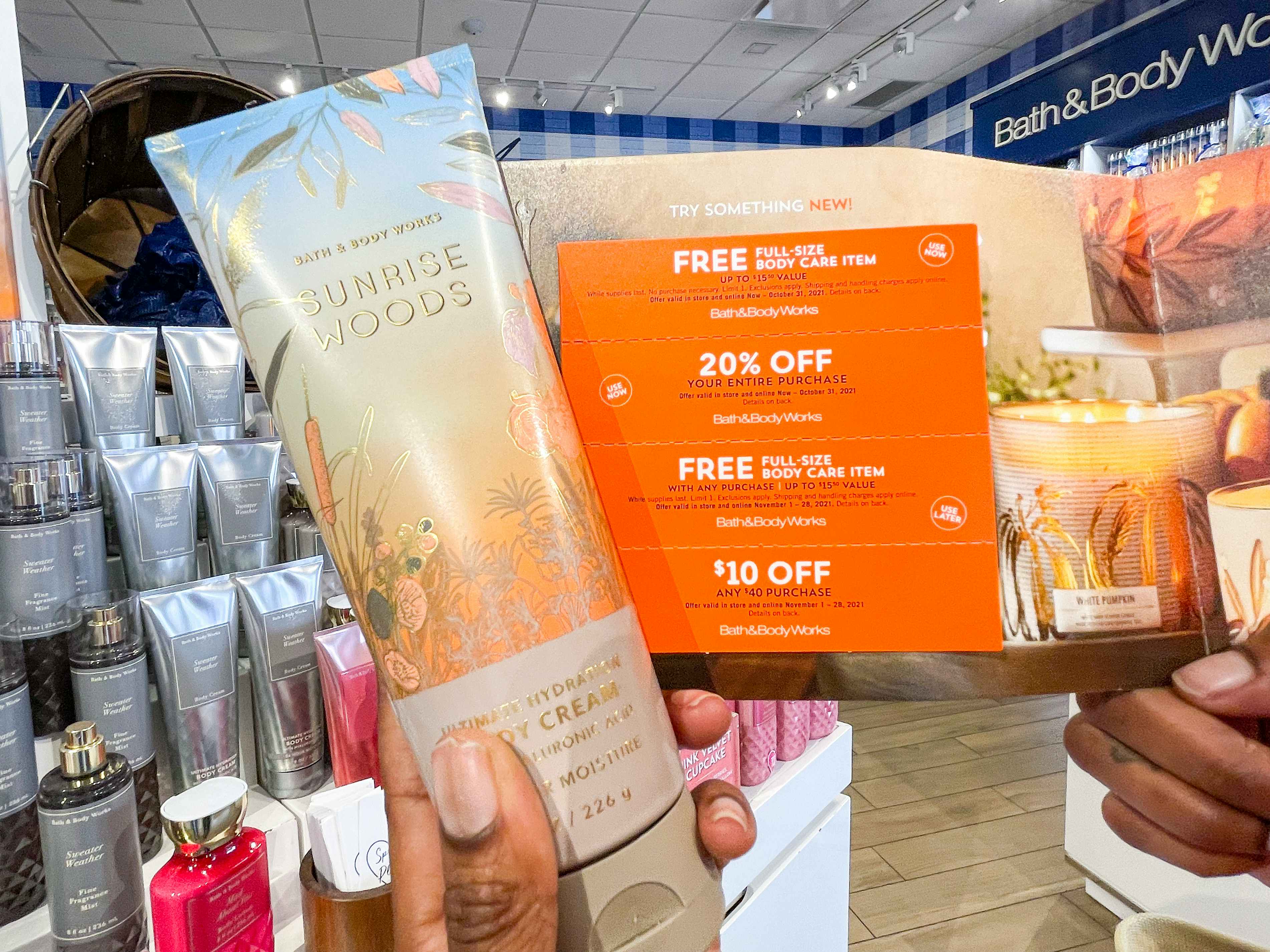 A person's hands holding a bottle of lotion and a card of coupons inside Bath & Body Works.