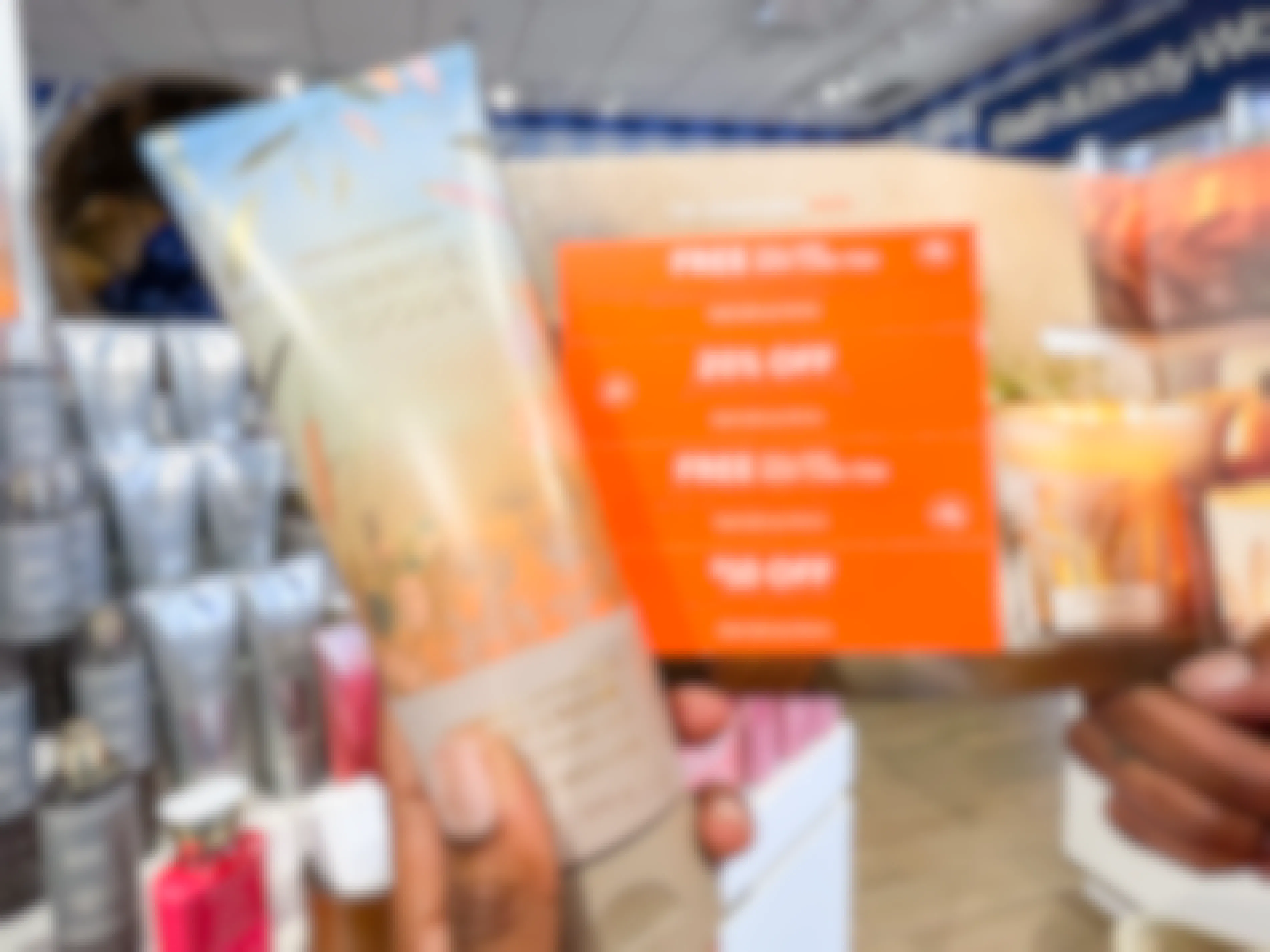 A person's hands holding a bottle of lotion and a card of coupons inside Bath & Body Works.