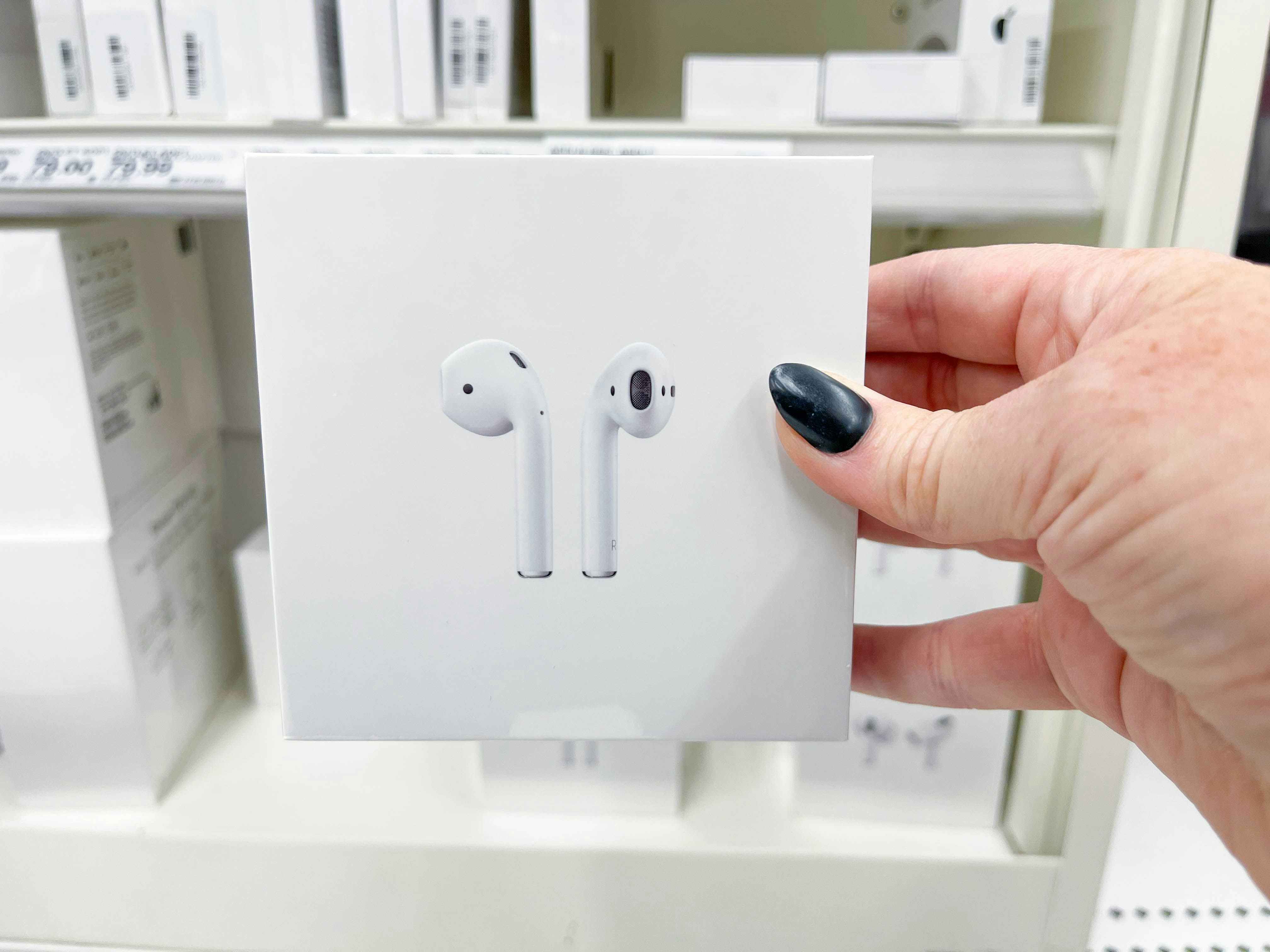 Someone holding a box of Apple Airpods in front of a shelf.